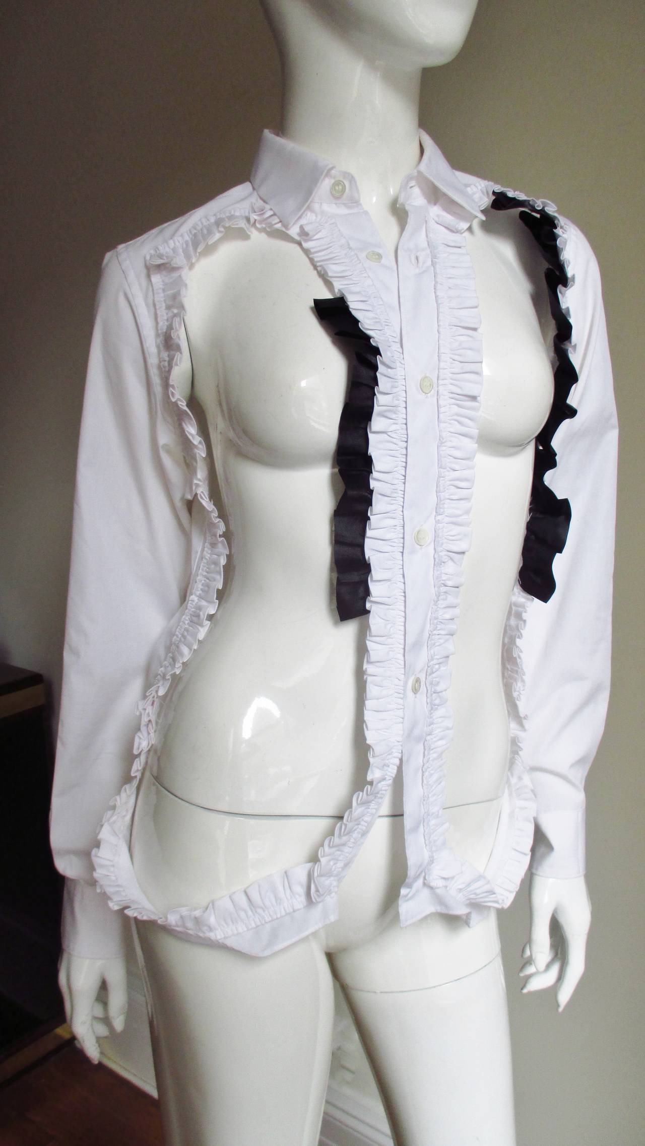 A fabulous black and white cotton avant garde shirt from Comme des Garcons CDG. It has long sleeves with button cuffs and is cutout on the from from shoulders to the hem with the exception of the front button placket. There are white ruffles and
