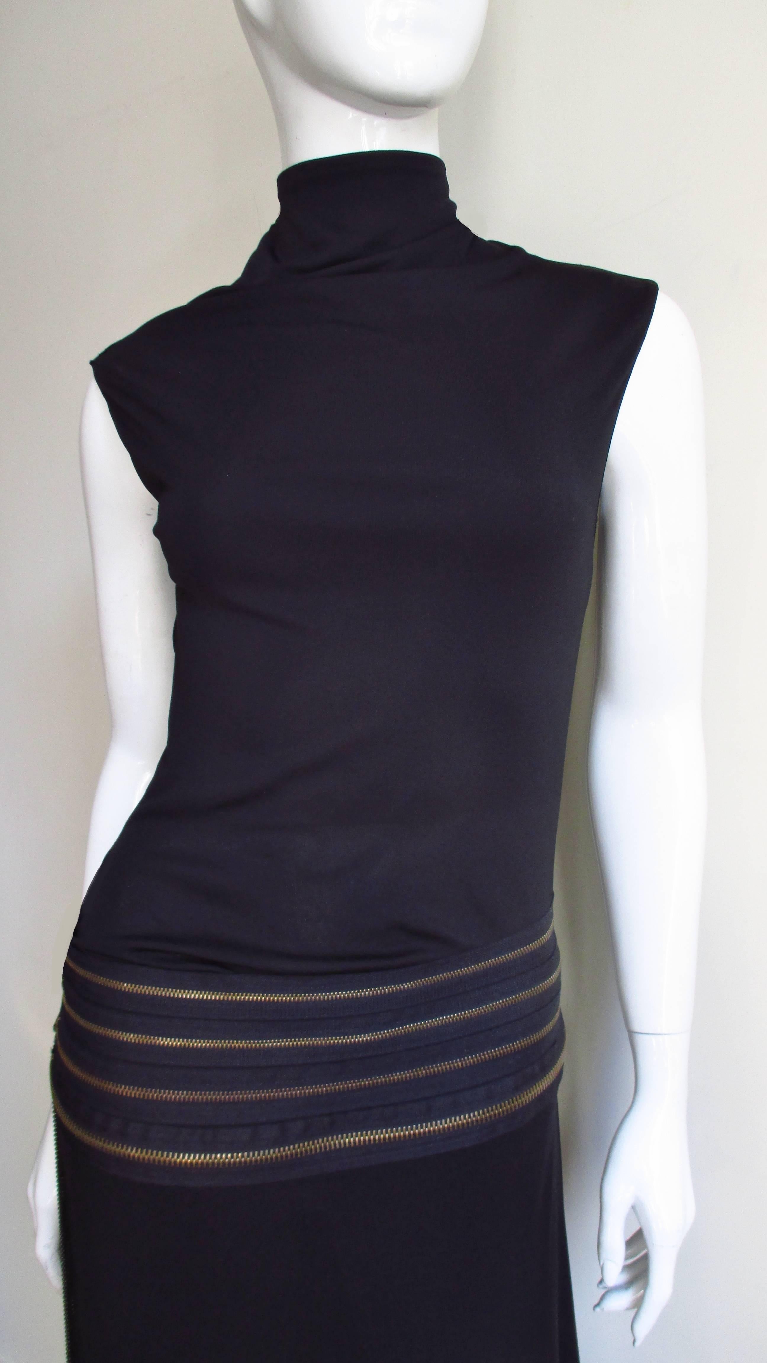 A fabulous black jersey dress from Jean Paul Gaultier.  It has elongated shoulders with a stand up collar and semi fitted through the top.  The hips are accentuated with a band of 4 horizontal functional zippers in burnished gold with long matching