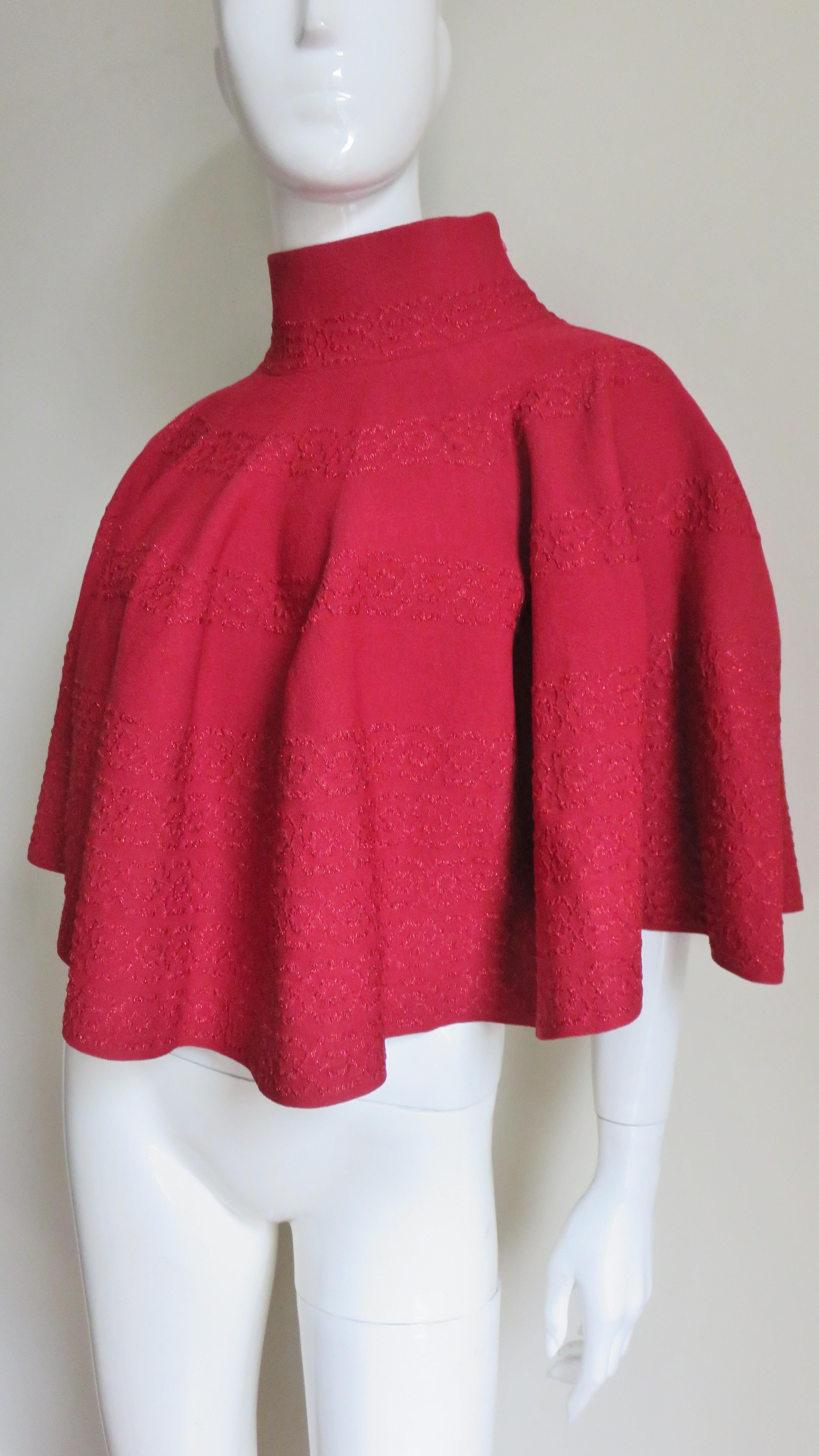 A fabulous red knit cape poncho by Azzedine Alaia.  It is elbow length with a stand up collar and a subtle abstract horizontal pattern in rows around the cape.  There is a zipper at the side of the neck and shoulder and it is unlined.
One Size Fits