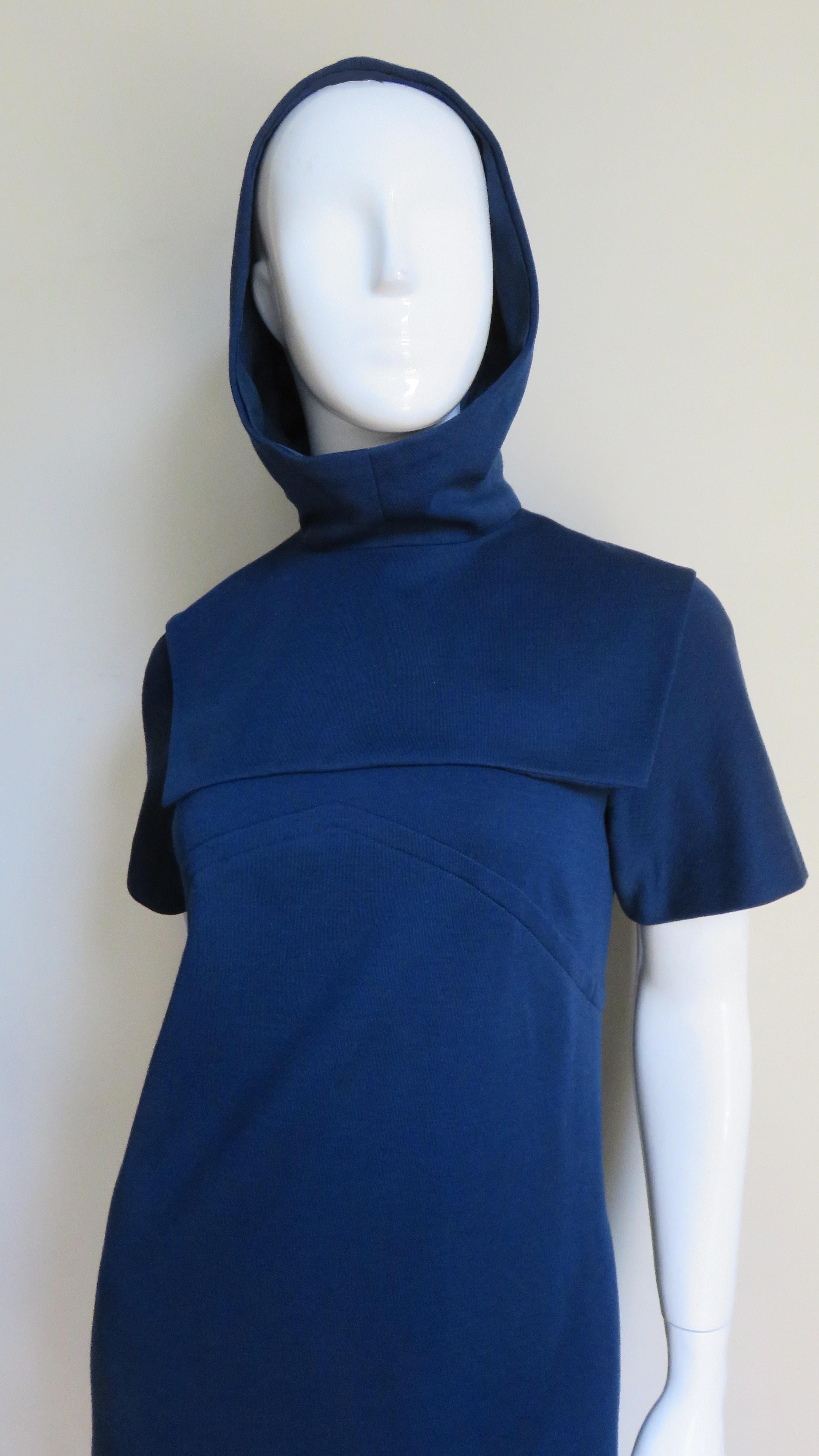 A blue wool jersey dress with a matching hood from Pauline Trigere. The dress has a simple crew neckline, short sleeves, an inverted V seaming at the upper chest and back plus a back zipper.  The matching separate hood slips on zipping closed up the