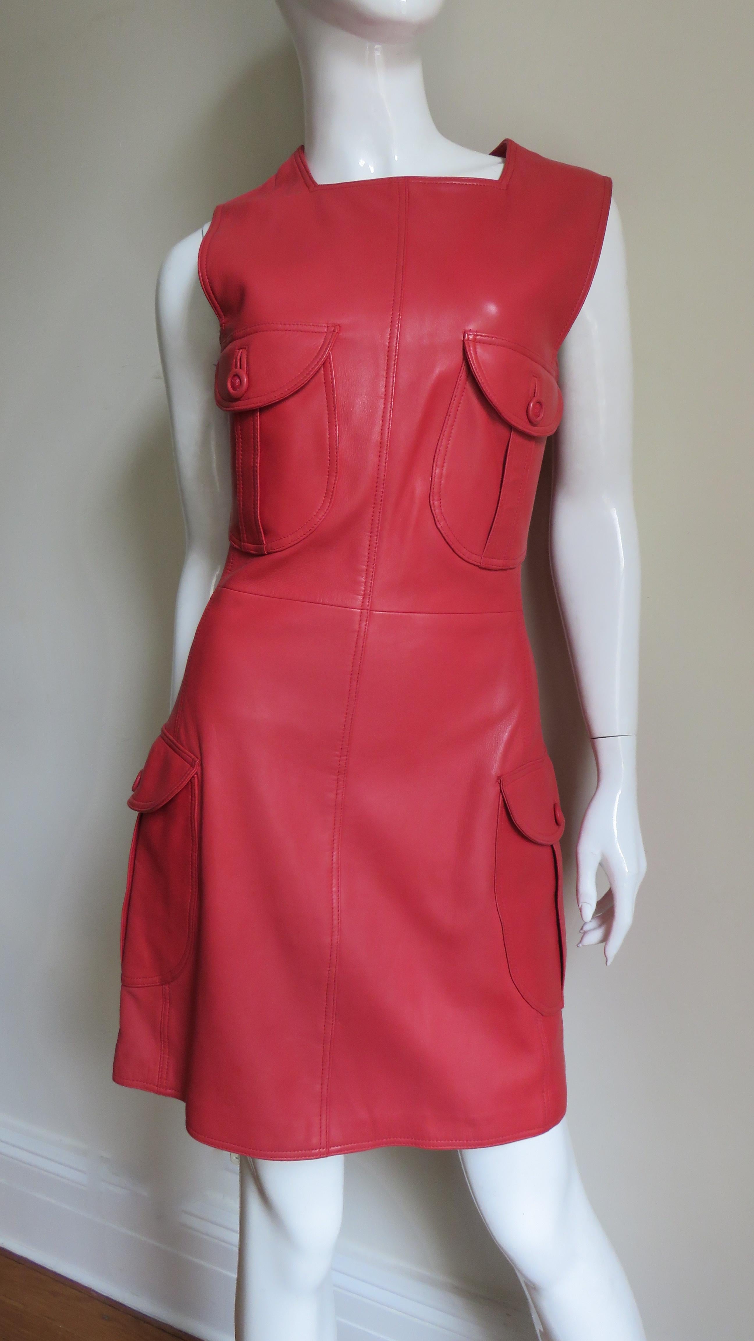 A fabulous red leather dress by Gianni Versace.  It is sleeveless with a squared neckline and armholes and flap patch pockets each with a large matching medusa head embossed button and a bound buttonhole- 2 on the front bodice and 2 on the skirt