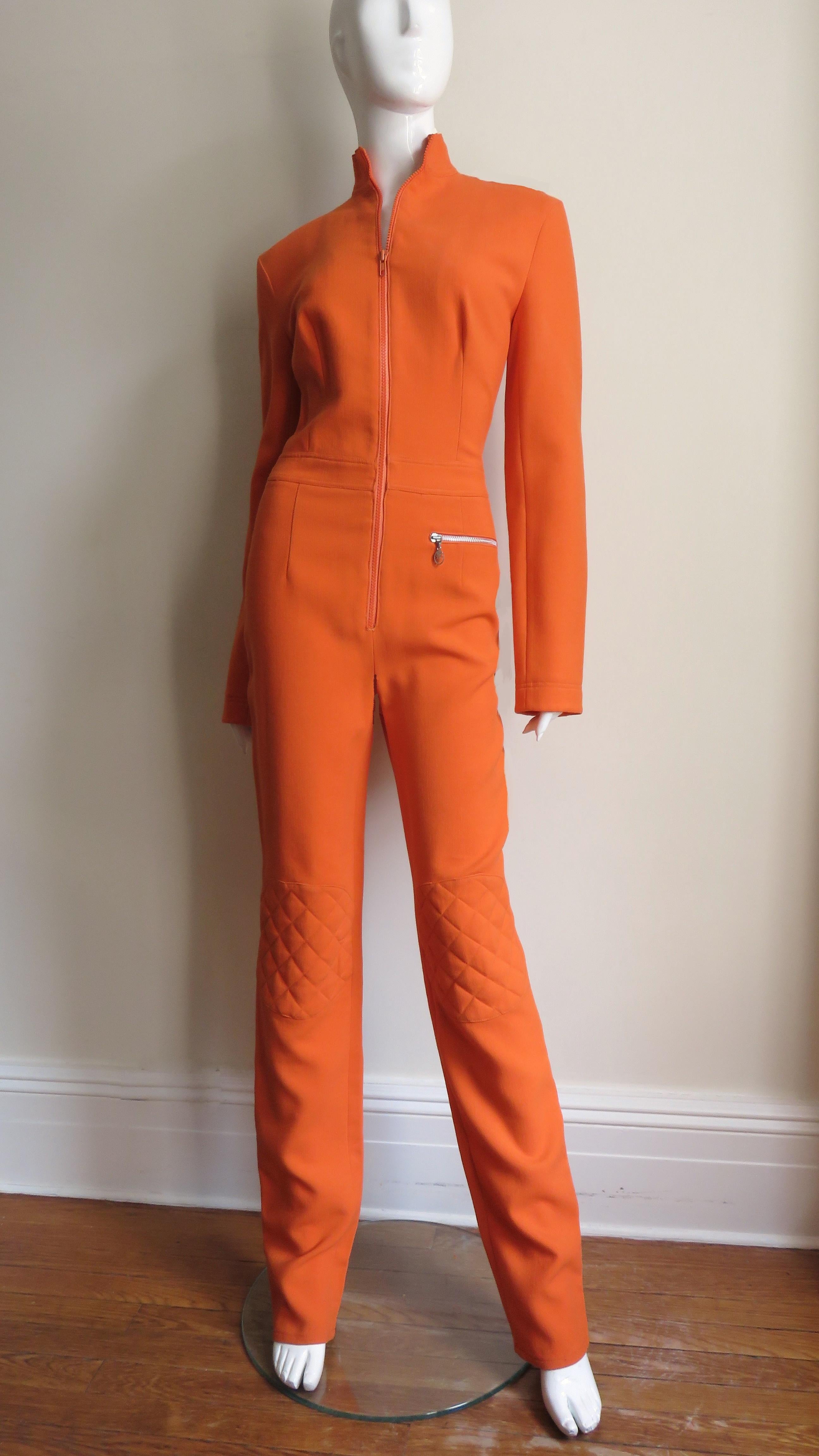 A fabulous orange wool jumpsuit from Jean Charles de Castelbajac.  It has a stand up collar, long sleeves with zippers at the wrists, a front hip zipper pocket and a large matching orange zipper up the front.  The elbows and knees of the straight