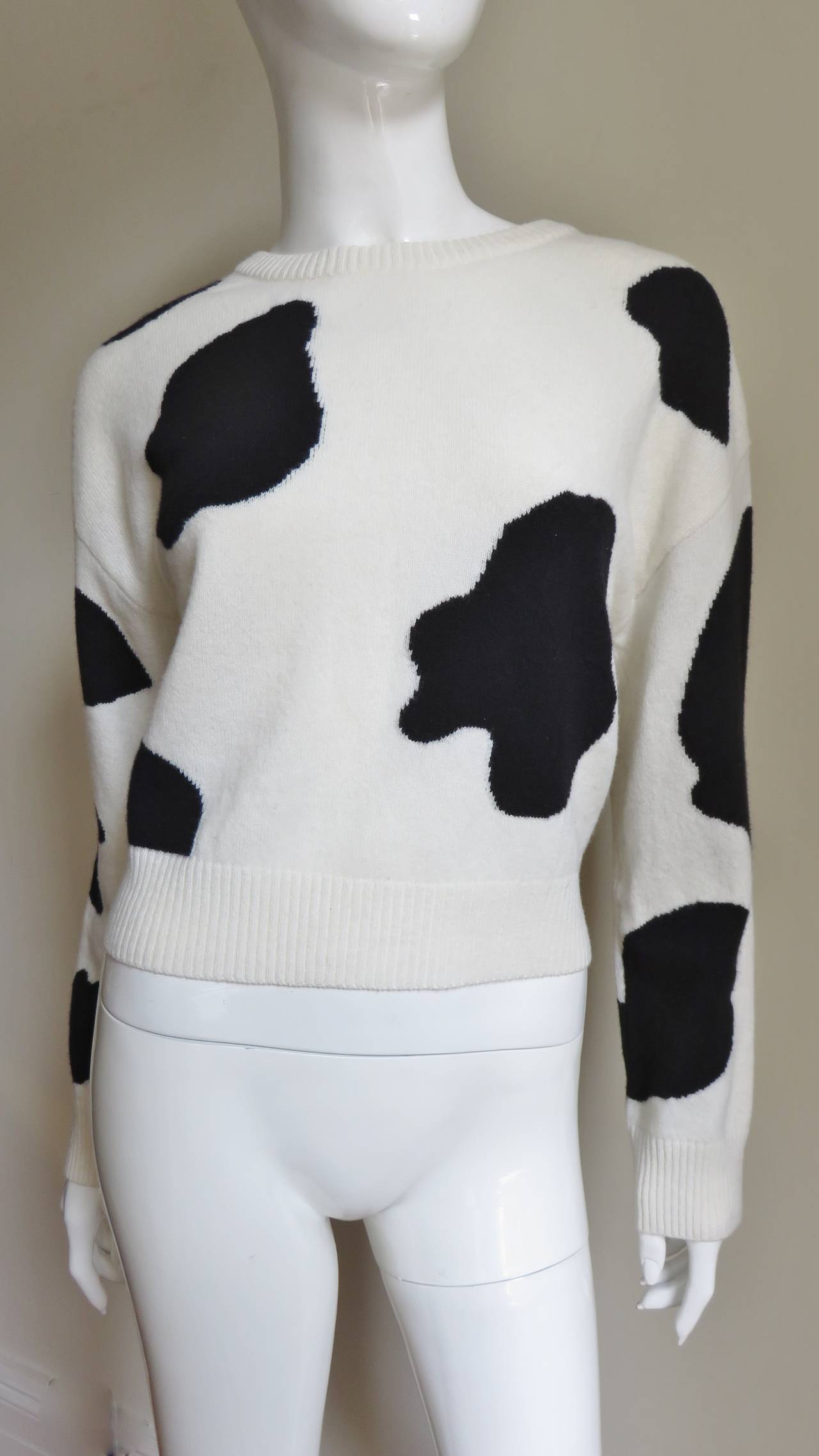 A fabulous whimsical off white and black cashmere sweater from Moschino Couture. It has long sleeves, a crew neckline and CASH COW emblazoned in gold capital letters individually appliqued onto the back of the cow hide pattern sweater.  It slips on
