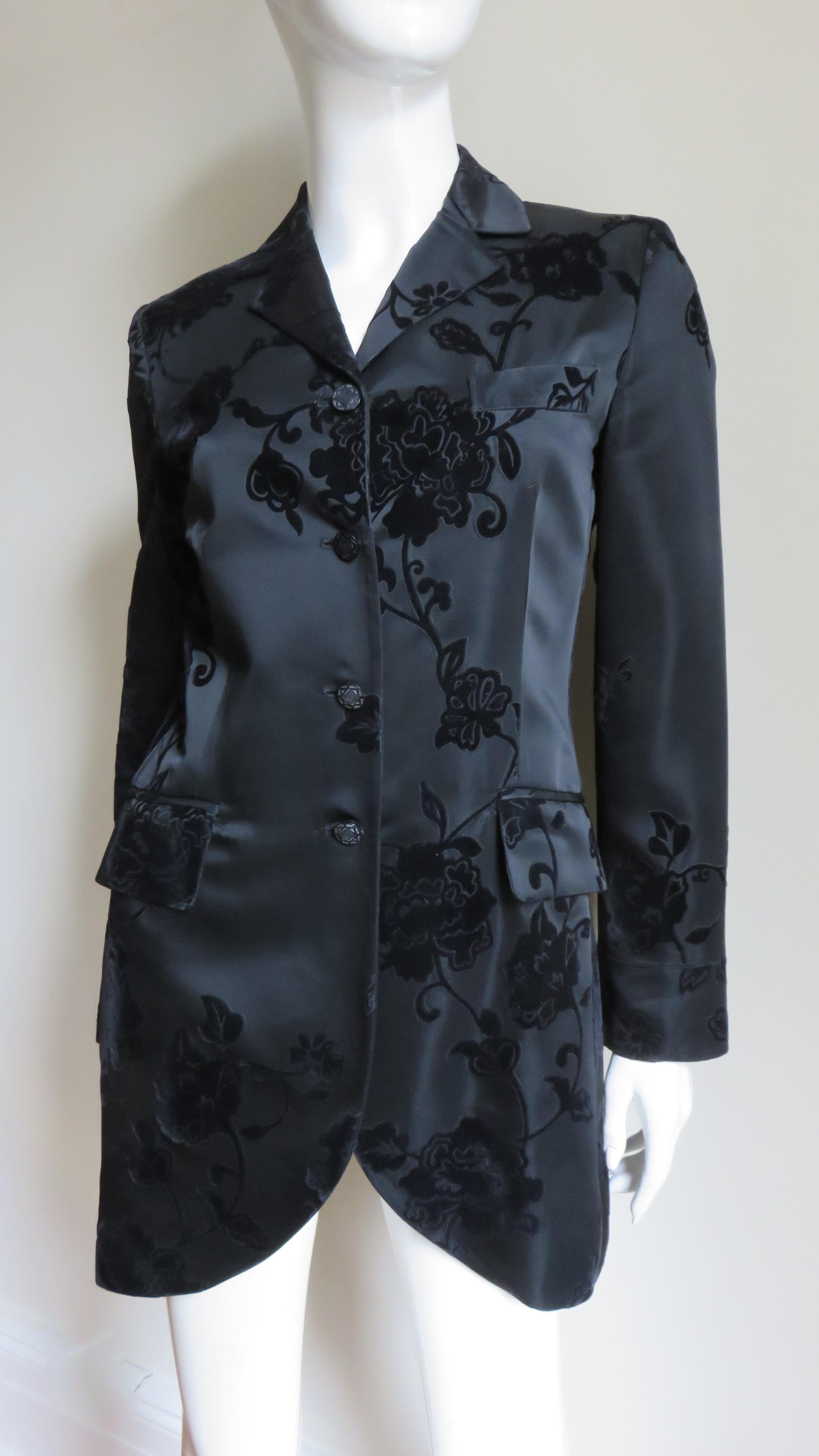 A beautiful black silk long single breasted jacket flocked with elaborate black velvet flowers by Alberta Ferretti.  It has a lapel collar, front button closure, button cuffs and 2 hip flap pockets.  It is fully lined in black silk.
Fits sizes