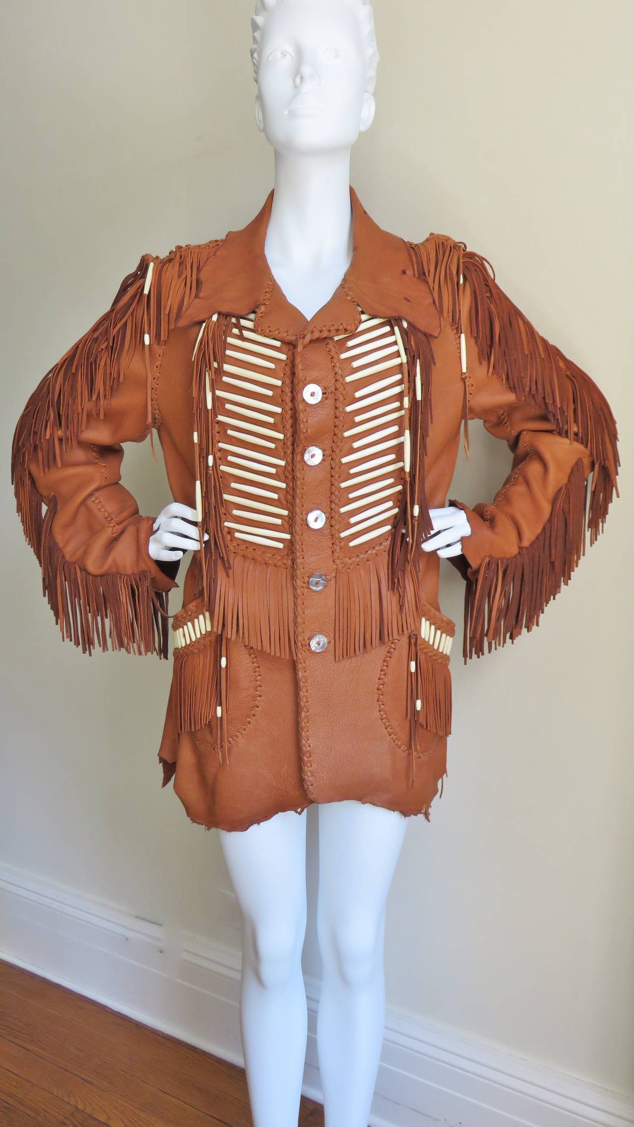 A stunning tan fringe leather jacket with carved bead detail handmade from Mahop.  The collar, cuffs and hem follow the natural lines of the hide, the other edges and seaming are highlighted with intricate hand braided and knotted strips of leather.