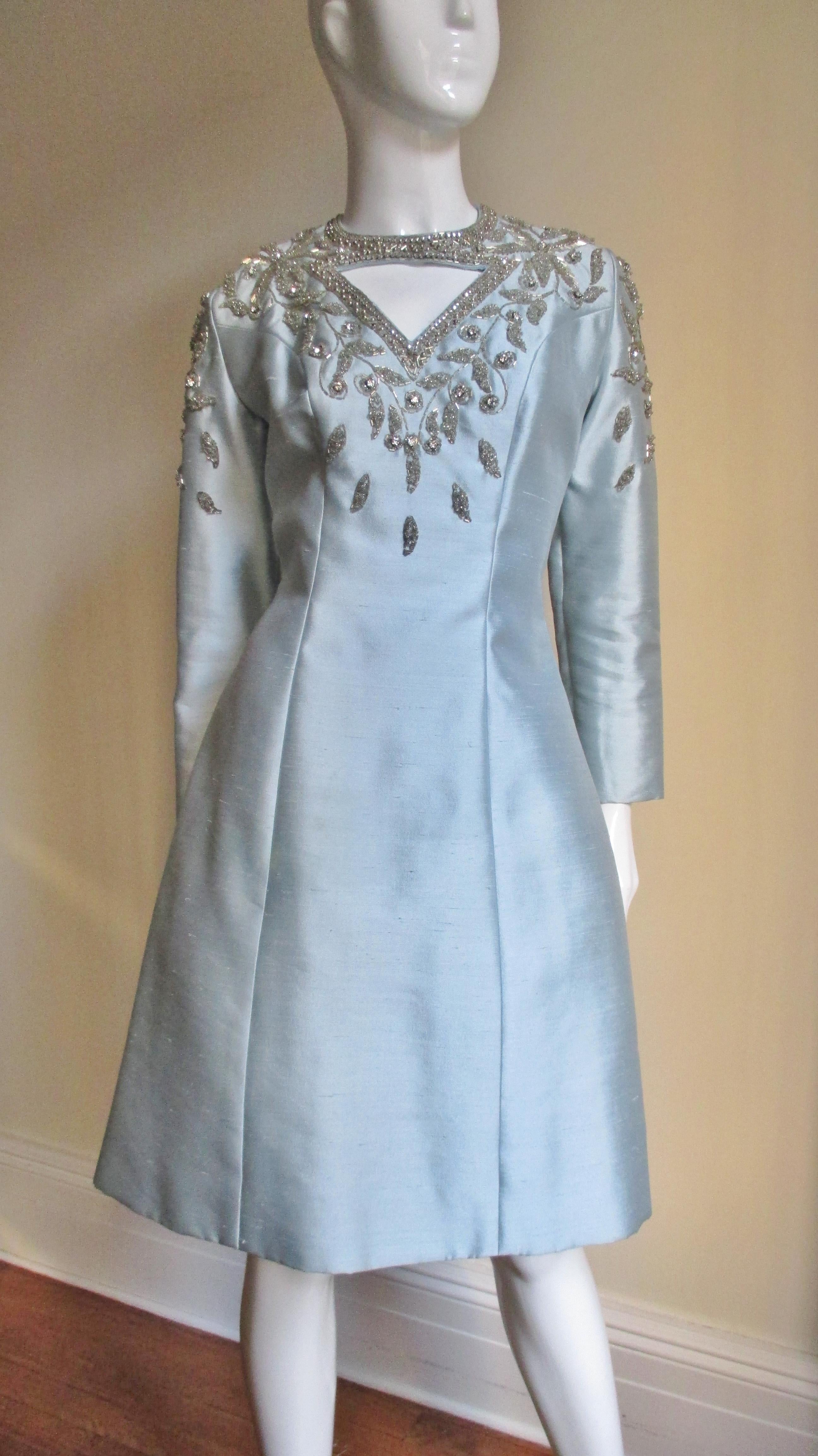 A beautiful pastel blue silk beaded dress from Bernetti, New York.  It has princess seaming for shaping with triangular cutouts just below the neck front and back.  Both are outlined in prong set rhinestones and elaborately framed in silver tubular