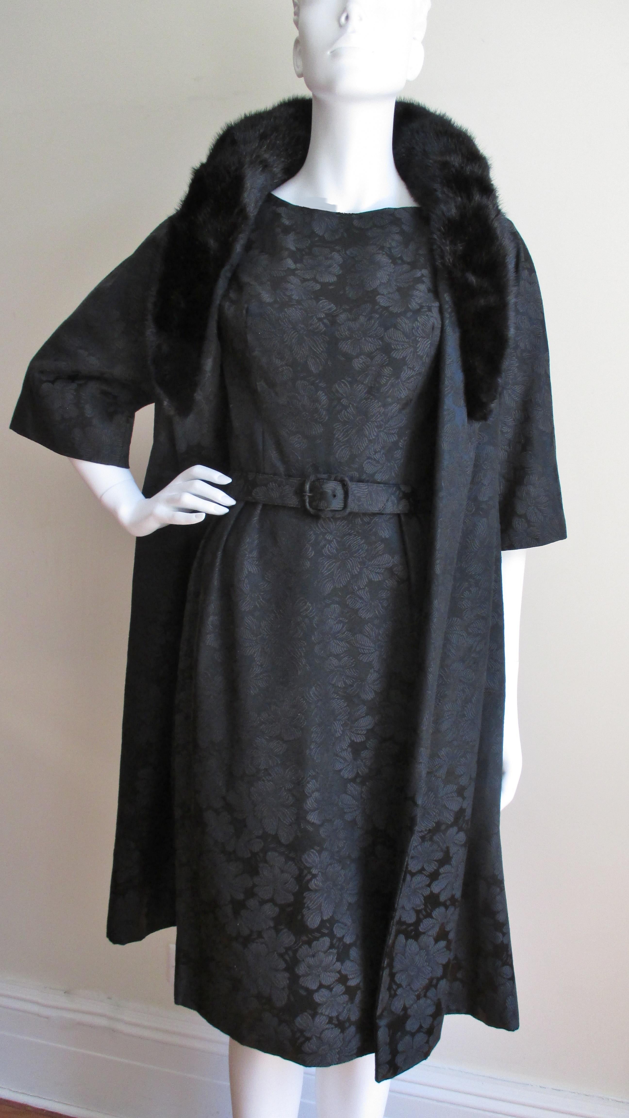 A rare, new 1950s dress and coat set from Lillie Rubin in a black silk damask flower pattern. The dress is semi fitted with a matching belt, a bateau neckline, and a straight skirt. The elbow length raglan sleeve coat falls from the shoulders in an