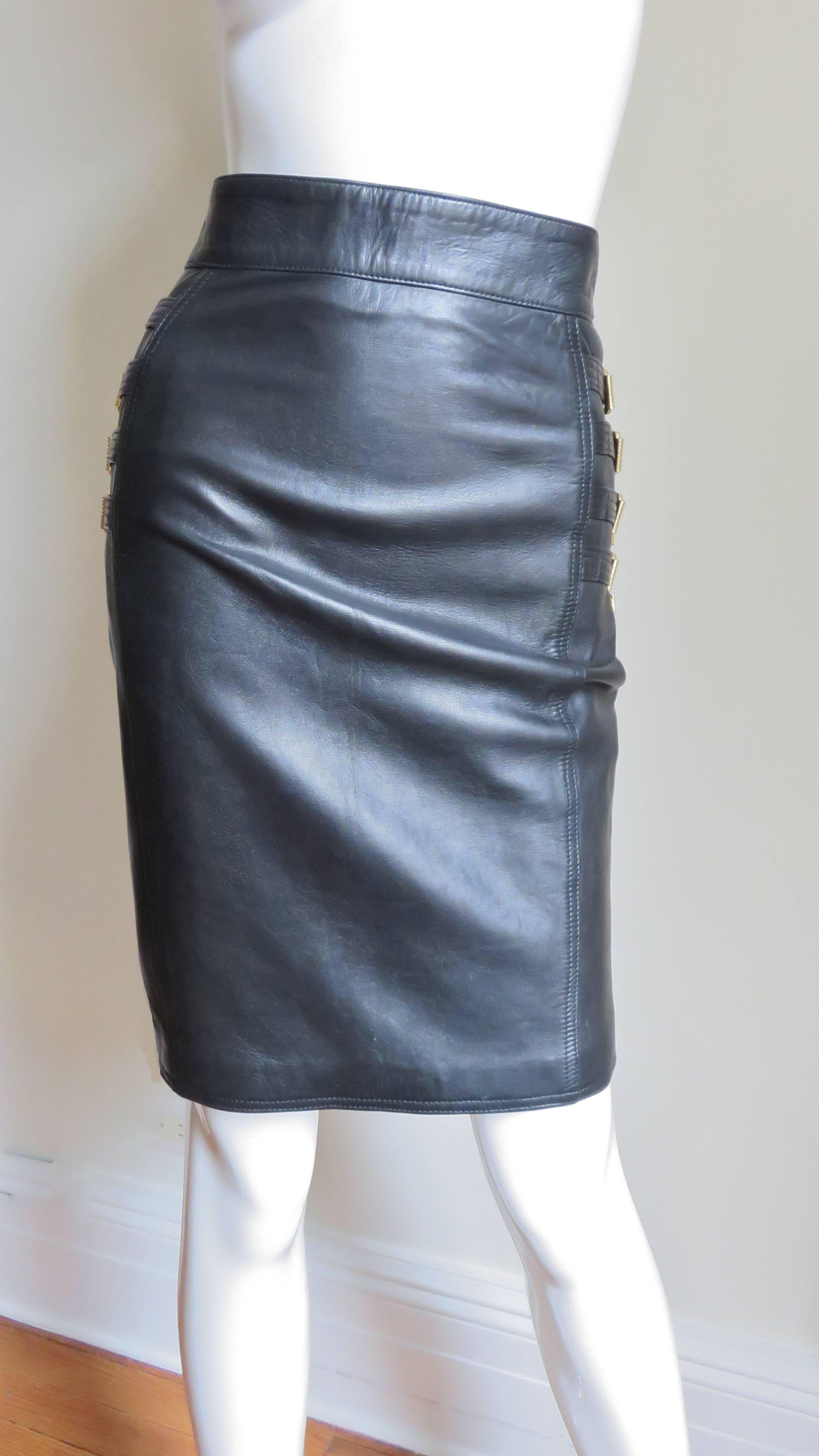 A soft, supple, black leather skirt from Gianni Versace's 1994 collection.  Each side of the hips is adorned with 4 intricately detailed multi top stitched functional, adjustable straps with gold metal buckles, tips and loops (each has one gold and