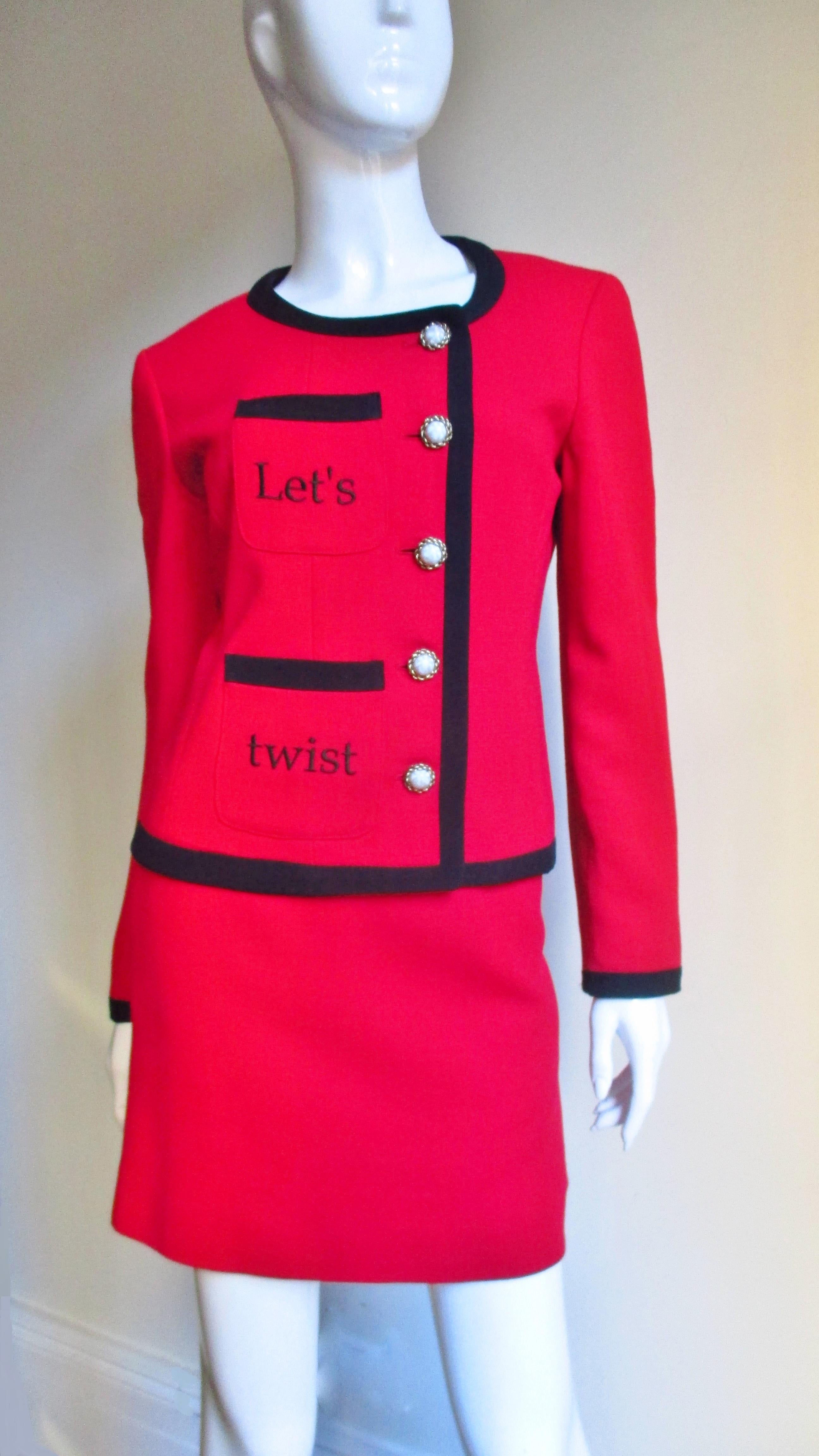 A fabulous red light weight wool skirt suit from Moschino. The hip length jacket closes off center with 5 pearl buttons and 2 pockets on one side above one another with the words 'Let's' and 'twist' embroidered in black.  The back has the same