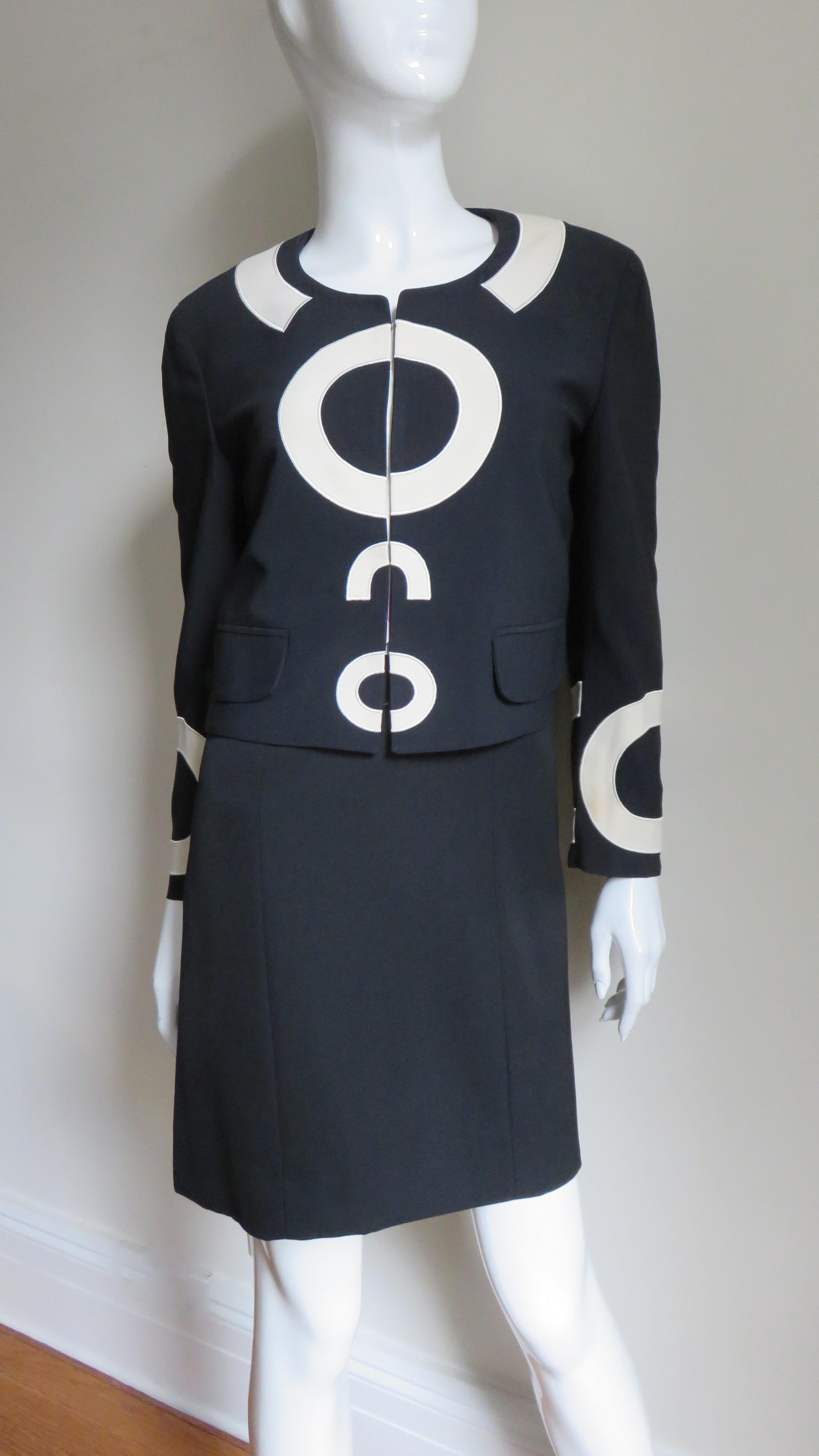 A fabulous dress and jacket set from Moschino Couture in black highlighted with off white silk appliqued lettering and graphics. The dress is a simple sleeveless shift with a crew neck and the words 'BE SIMPLE' appliqued on the front in large off