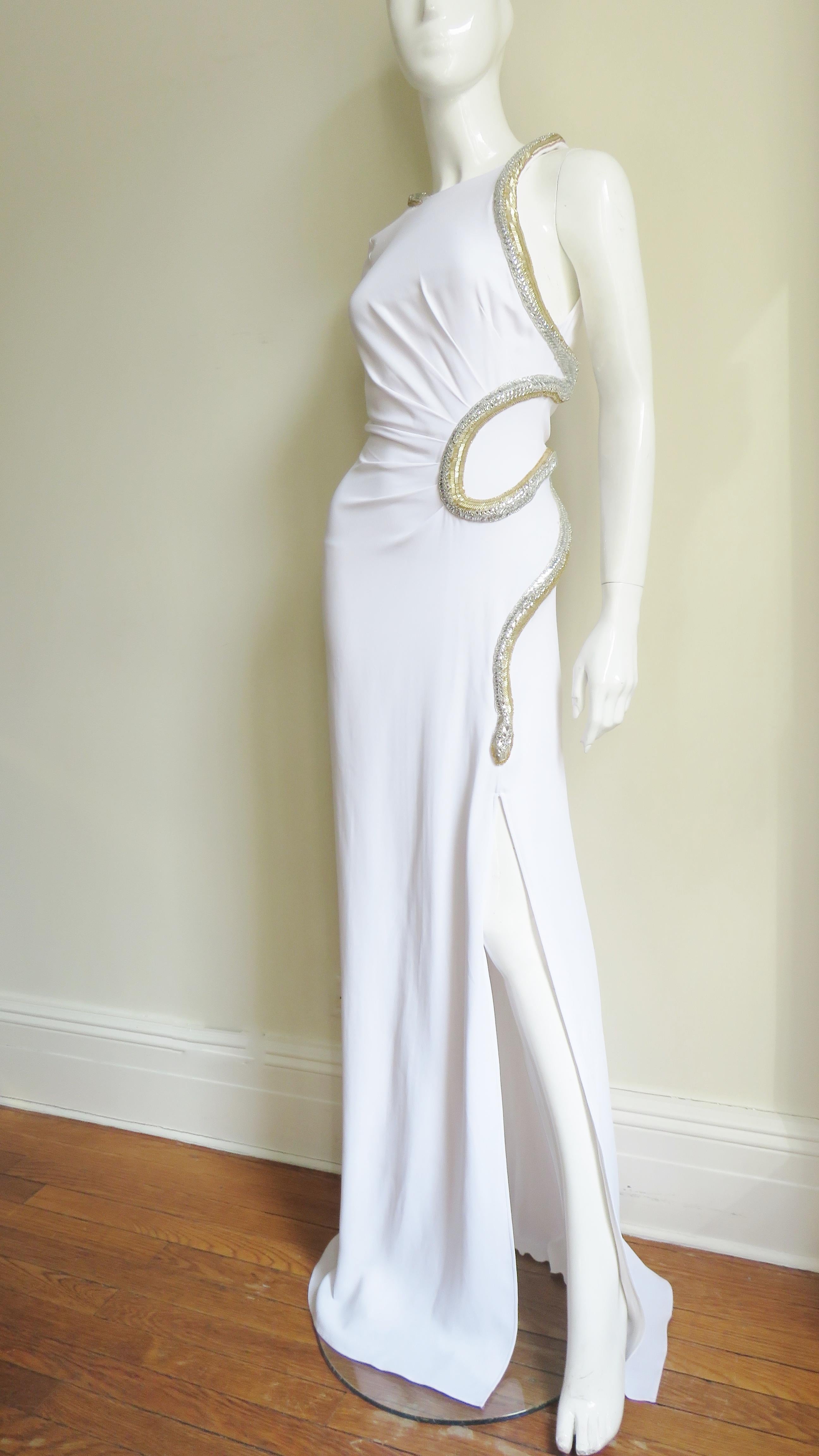 A gorgeous white silk gown with a bit of stretch for an enhanced fit from Roberto Cavalli.  It is fitted with one long zipper wrist sleeve. There is an elaborate glass beaded serpent in silver and gold wrapping around the back neck, along the front