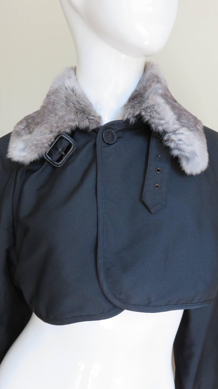 A beautiful black fur trimmed jacket from Jean Paul Gaultier.  It is cropped with a soft, fur trimmed collar in shades of grey and full raglan sleeves with matching wide fur cuffs.  The collar has a front button closure under a functional,