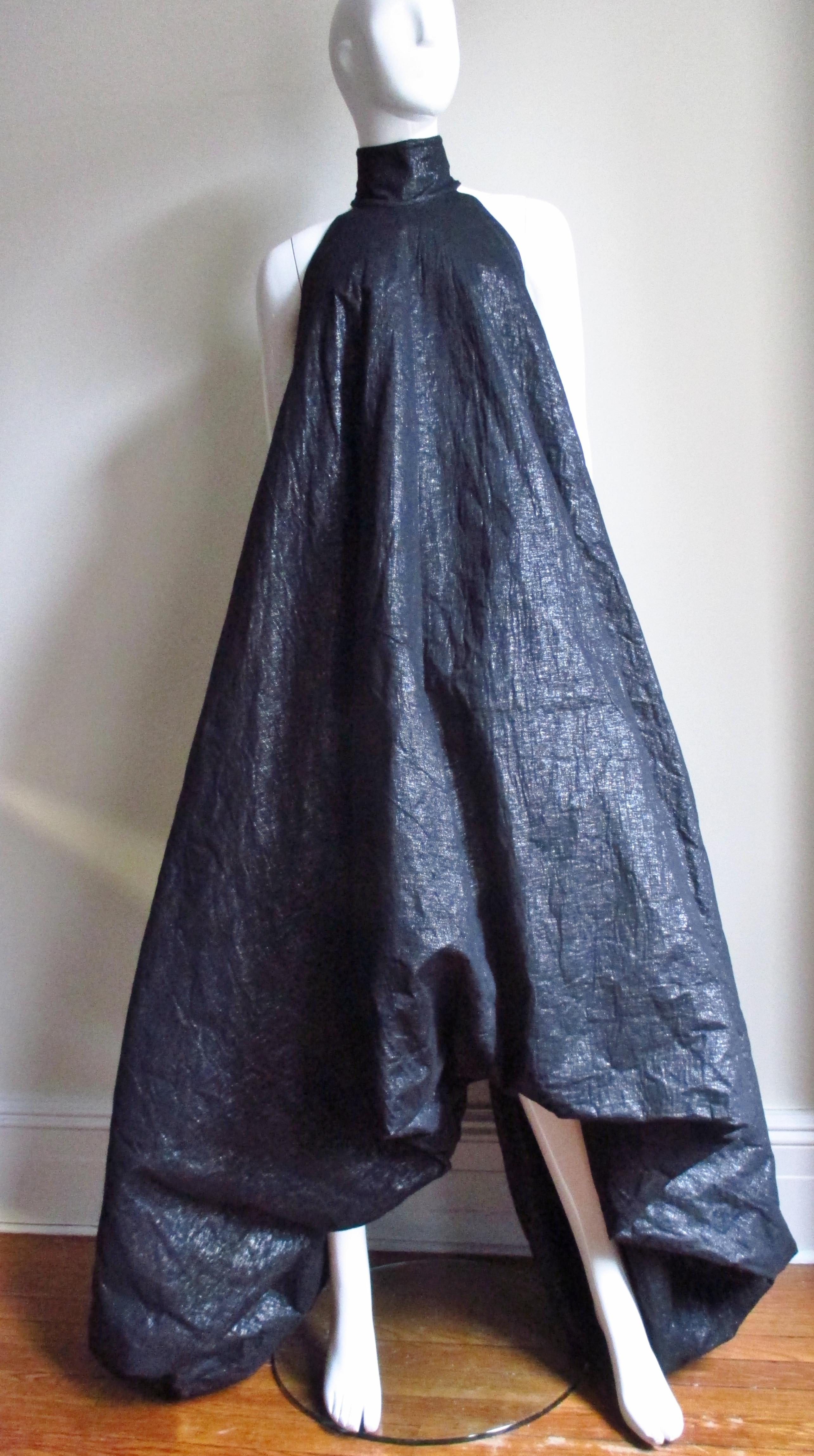 A fabulous maxi dress gown from Gareth Pugh in a black cotton/silk blend with a subtle shine. The silhouette is dramatic- narrow at the stand up collar and cut in shoulders then becoming wider towards the hemline which is shorter in the center front