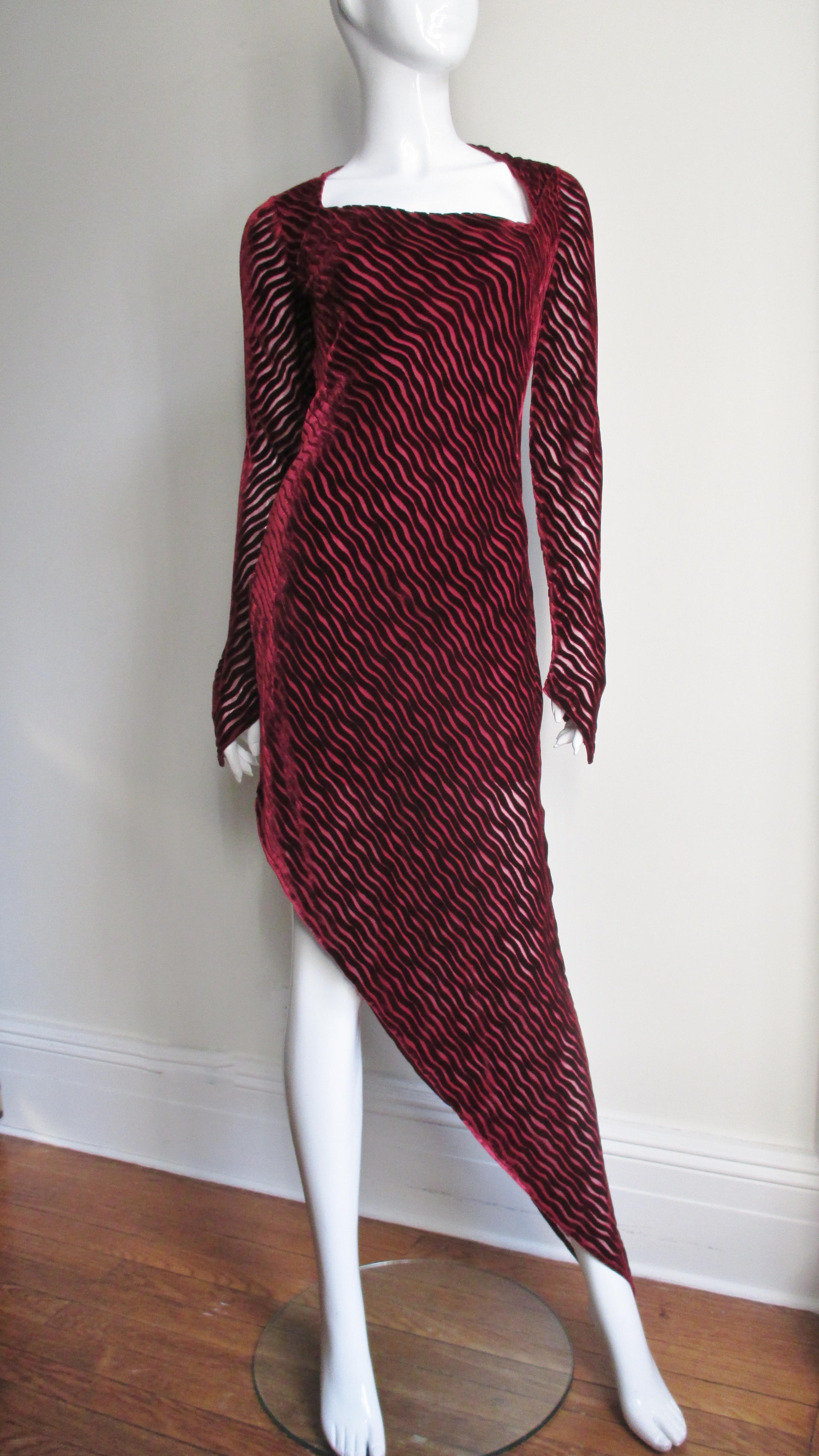 A fabulous dress from Karl Lagerfeld in burnout Bordeaux silk velvet alternating wavy lines with sheer.  It has an asymmetric square neckline, long sleeves with pointed cuffs over the hands and a hemline cut at an angle.  It has a matching side