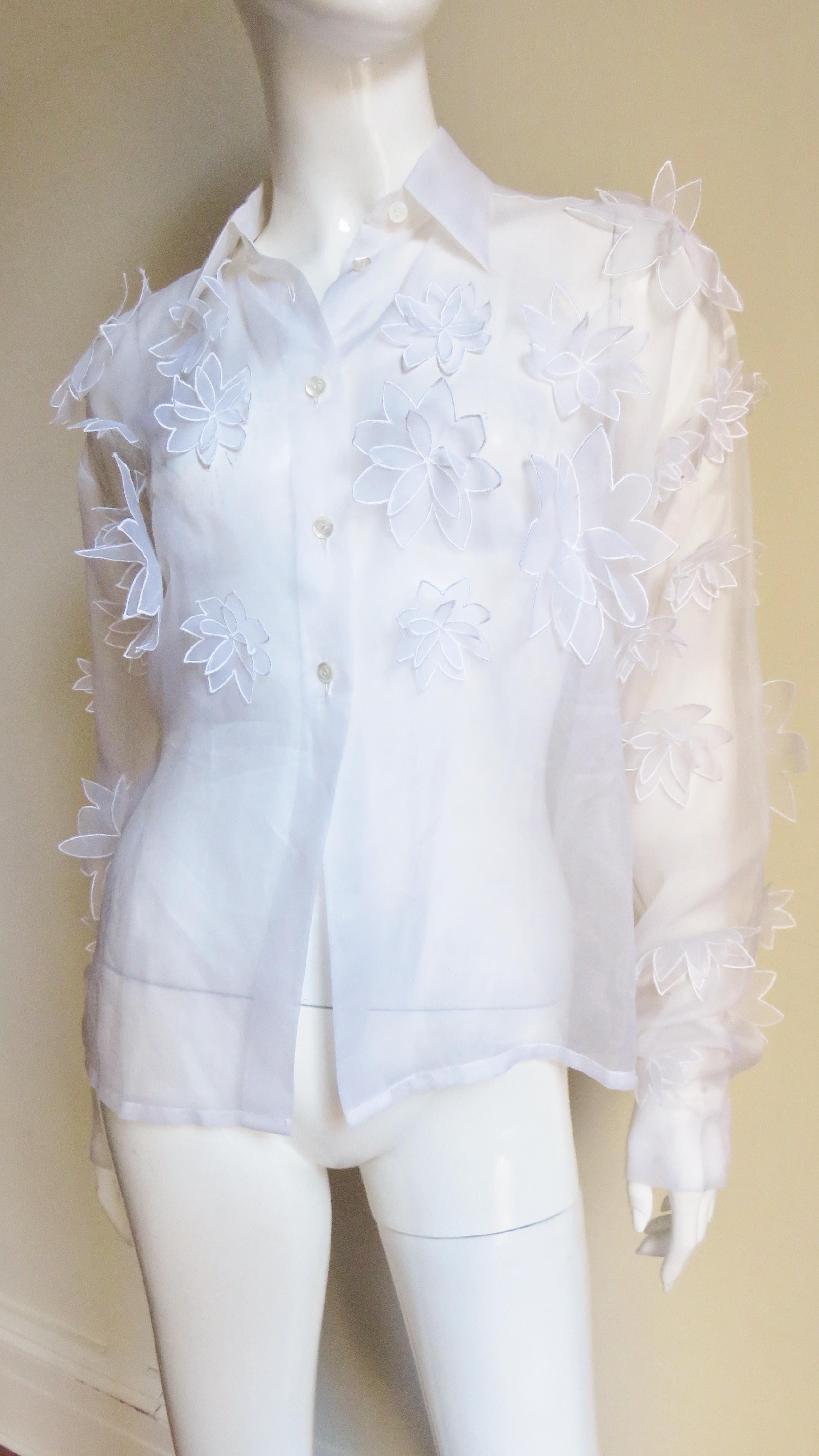 A stunning white semi sheer silk shirt, blouse from Dolce & Gabbana.  It has a shirt collar and long sleeves with button cuffs.  The sleeves, upper front and back are covered in appliques of layered varying sized flowers in the same fabric each