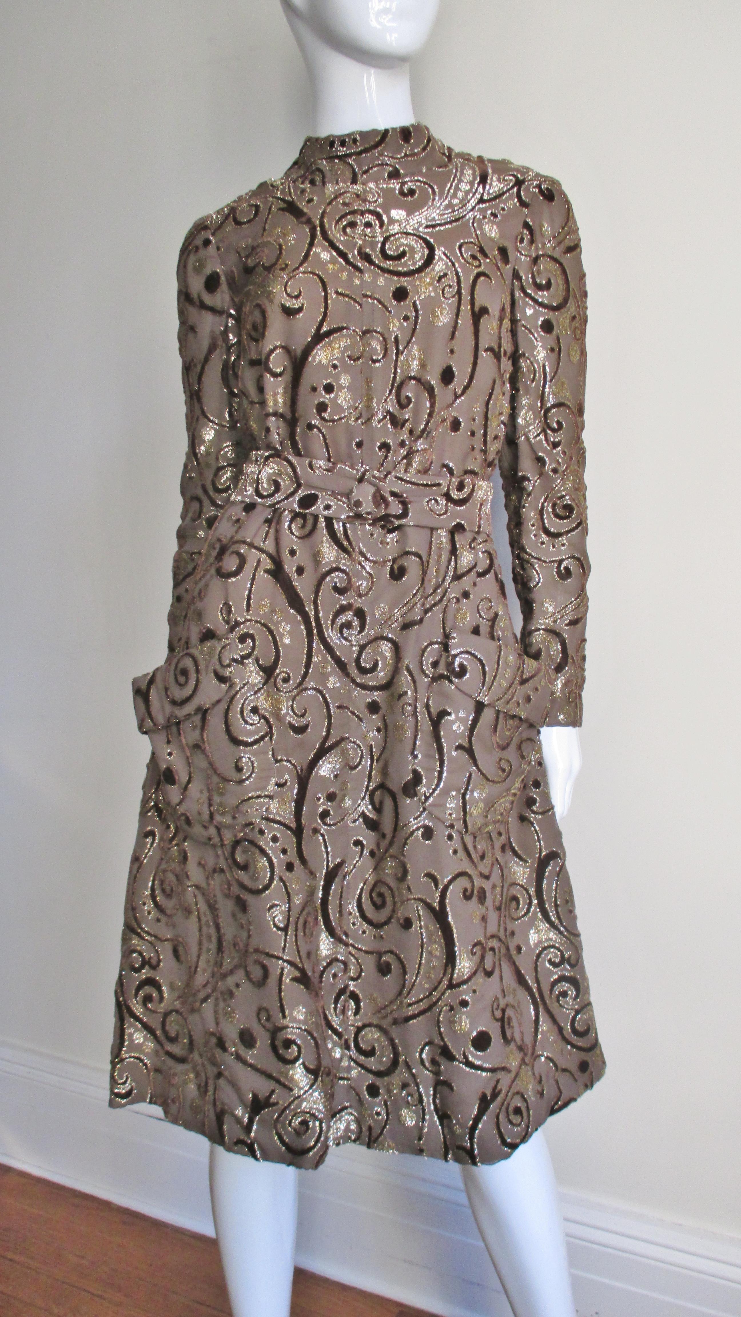 A taupe silk dress and matching belt with a cut velvet scroll and circle pattern outlined in gold from renowned American designer Pauline Trigere. The dress flares from shoulder to hem and looks attractive with or without it's matching belt. It has