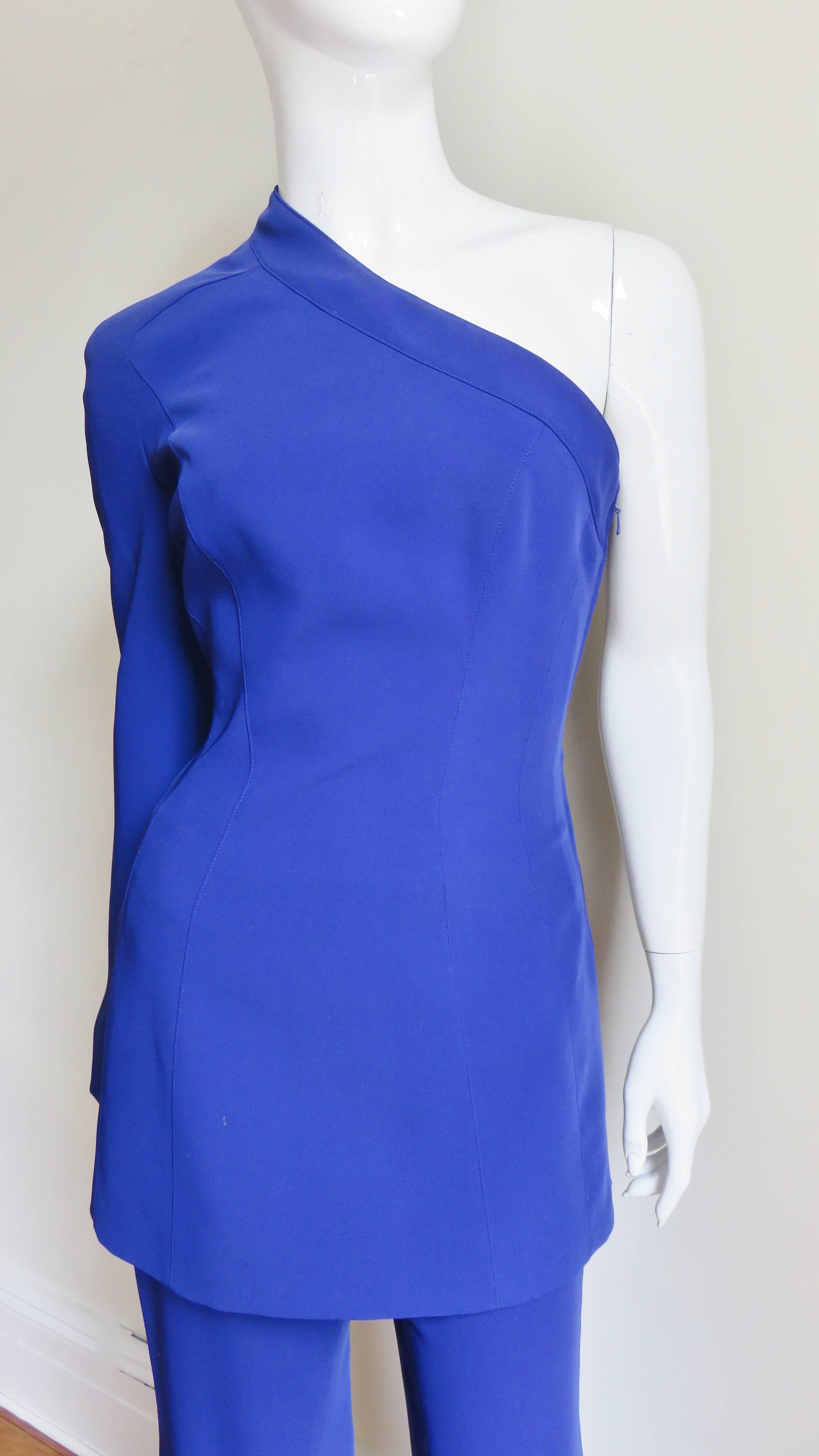 A clever and unique purple pant suit from Thierry Mugler.  It is comprised of a long jacket over full leg pants with a back zipper.  The tunic jacket has long bell sleeves, one which snaps into place and is removable. It has a side separating zipper