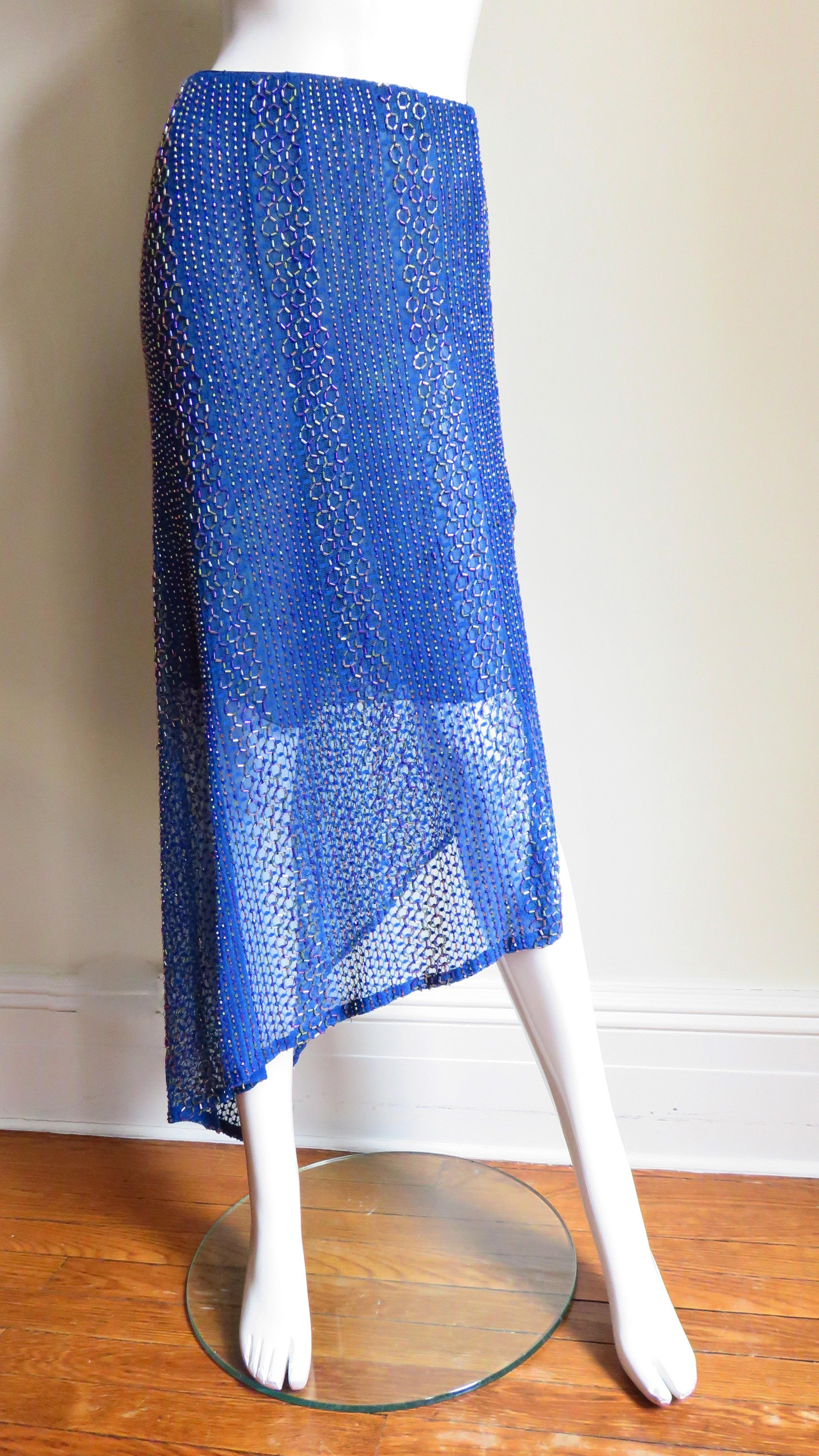A beautiful bright blue asymmetric stretch silk mesh skirt from Ordinary People.  The skirt has an asymmetric hemline and is covered in pink, blue and grey glass tubular and seed beads in rows of lines and small circles. It is lined to the knee in