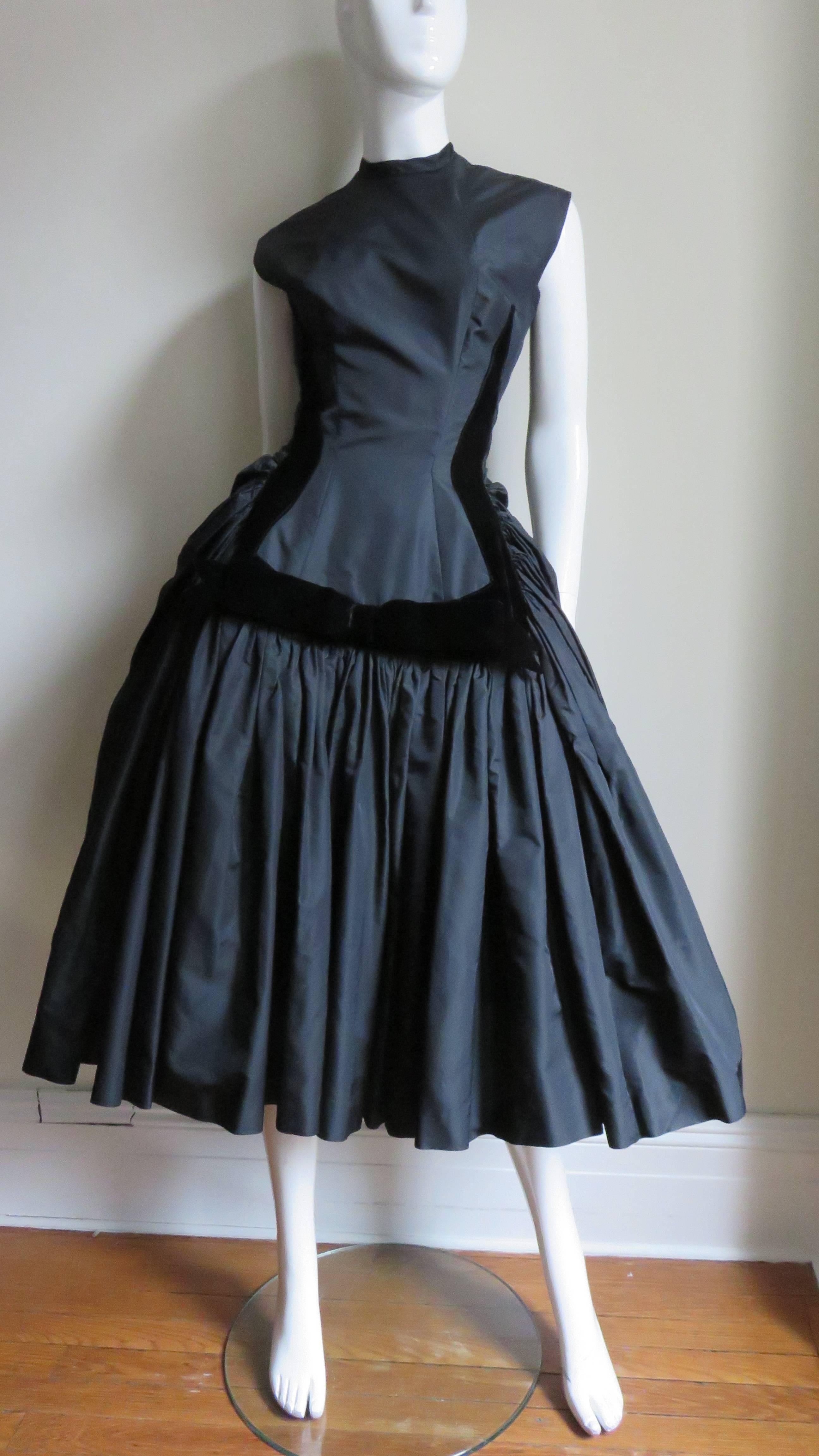 A fabulous black silk 1950s dress from Neusteters.  It is sleeveless with a fitted bodice, a crew neck, and a full gathered skirt. The front skirt panel is framed with black silk velvet. It is absolutely gorgeous!  It has a painted metal back zipper