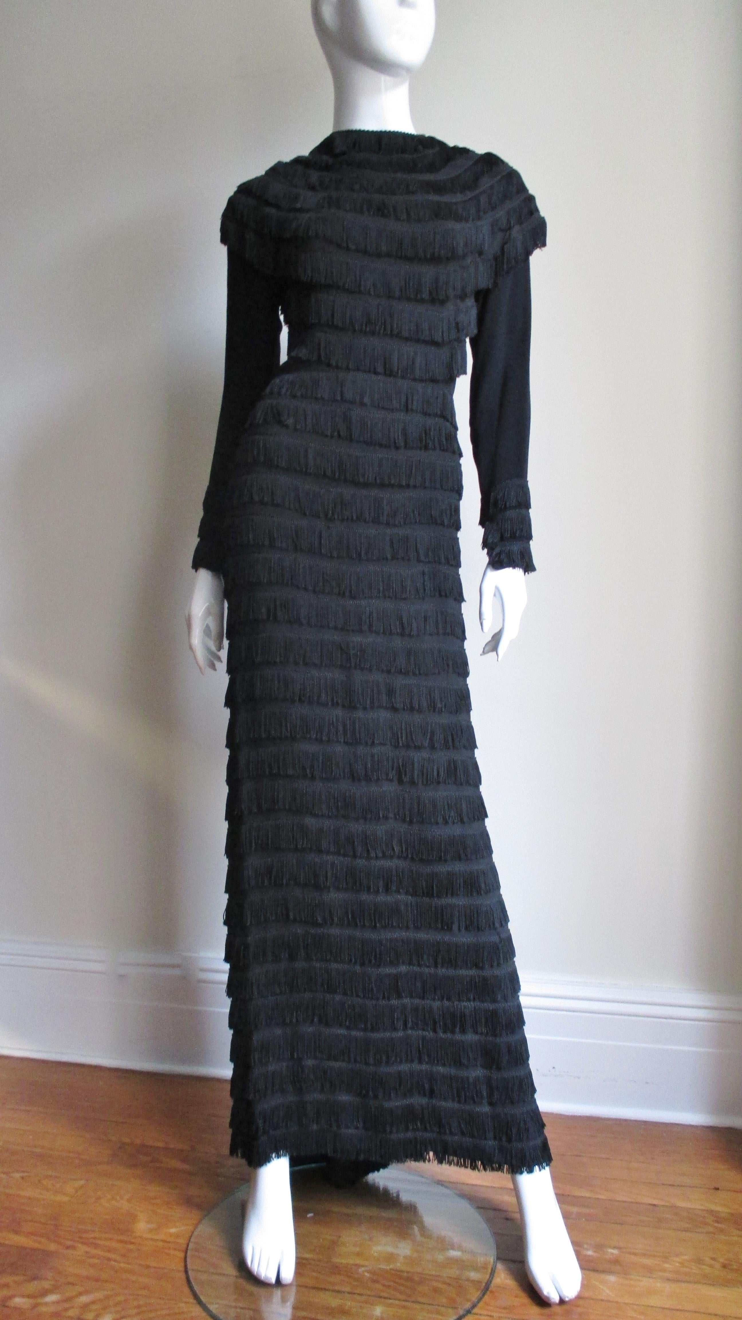 An extraordinary black silk 1930s dress completely covered in rows of fringe.  It has long sleeves and a rounded front and back yoke which extends over the shoulders and tops of the sleeves.  The dress is fitted from the front falling straight to