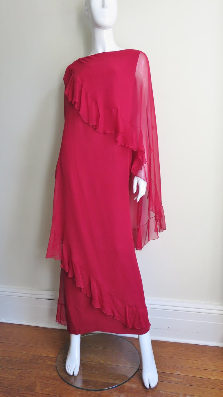 A fabulous dress in a deep red sheer silk from Jean Louis.  It is a sleeveless semi fitted full length sheath with a sheer ruffle hemmed attached draping winding twice around the dress at an angle starting at one shoulder ending finally at the front