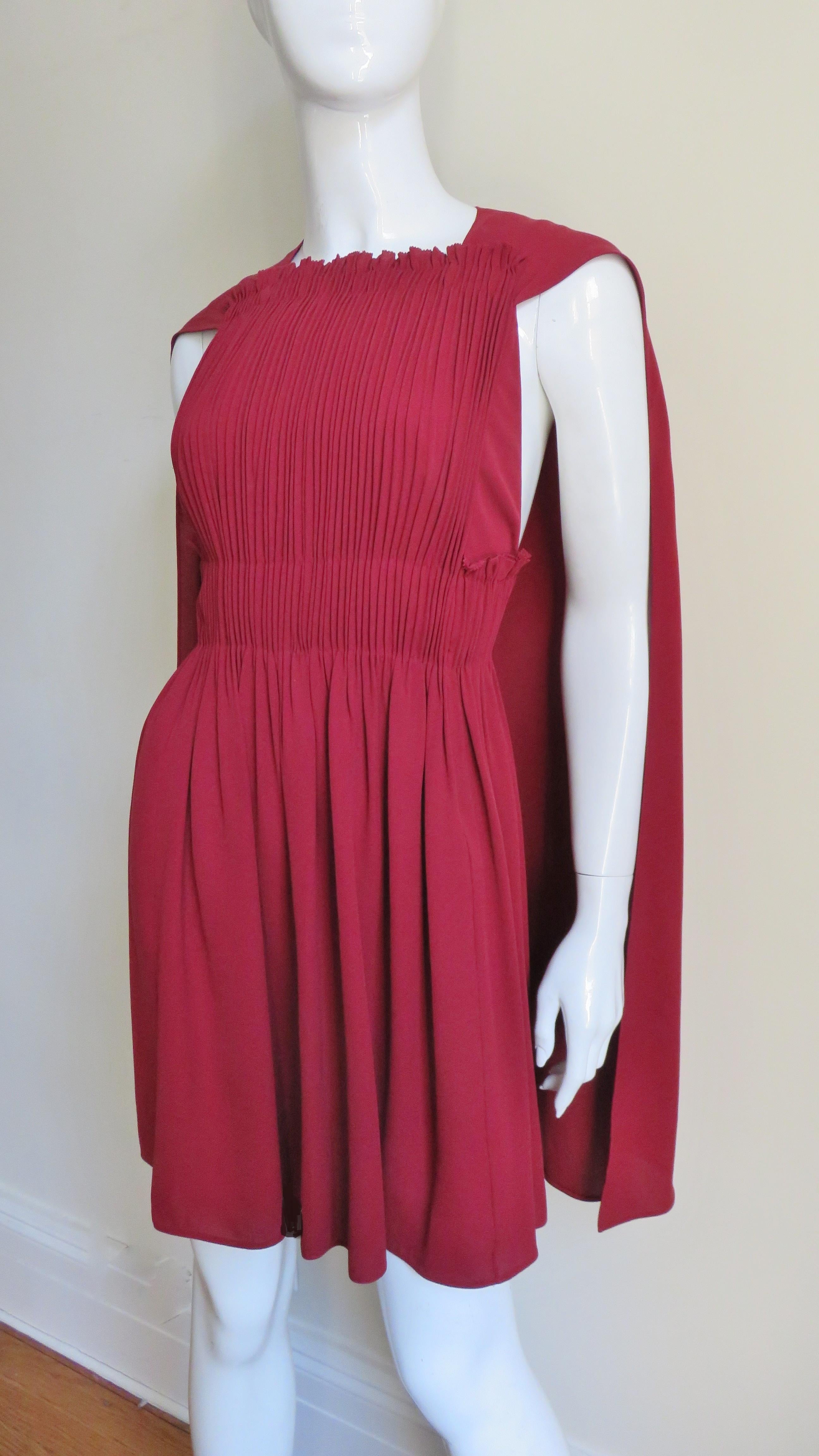 A fabulous deep red silk dress with an attached cape from Valentino. It has an elaborately vertically ruched front bodice with a back cape emanating from the shoulders and a full skirt. It is lined in matching silk, the dress has a back zipper and