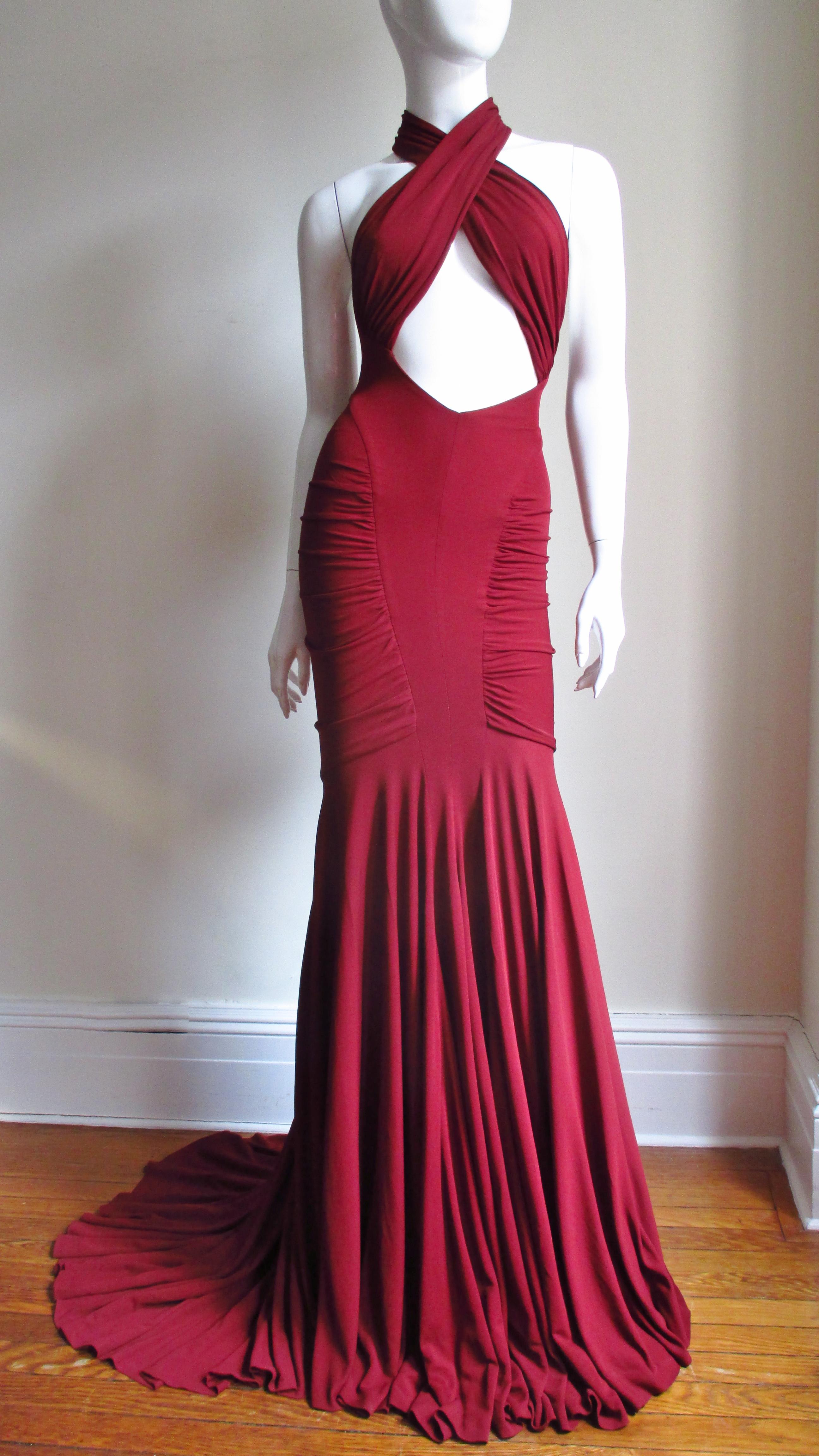 A stunning burgundy fine silk jersey gown by Guy Laroche. It has panels from the side waist crossing the bust, wrapping around the neck leaving a cut out midriff and cut in shoulders in the back.  The skirt has center front and back knee length