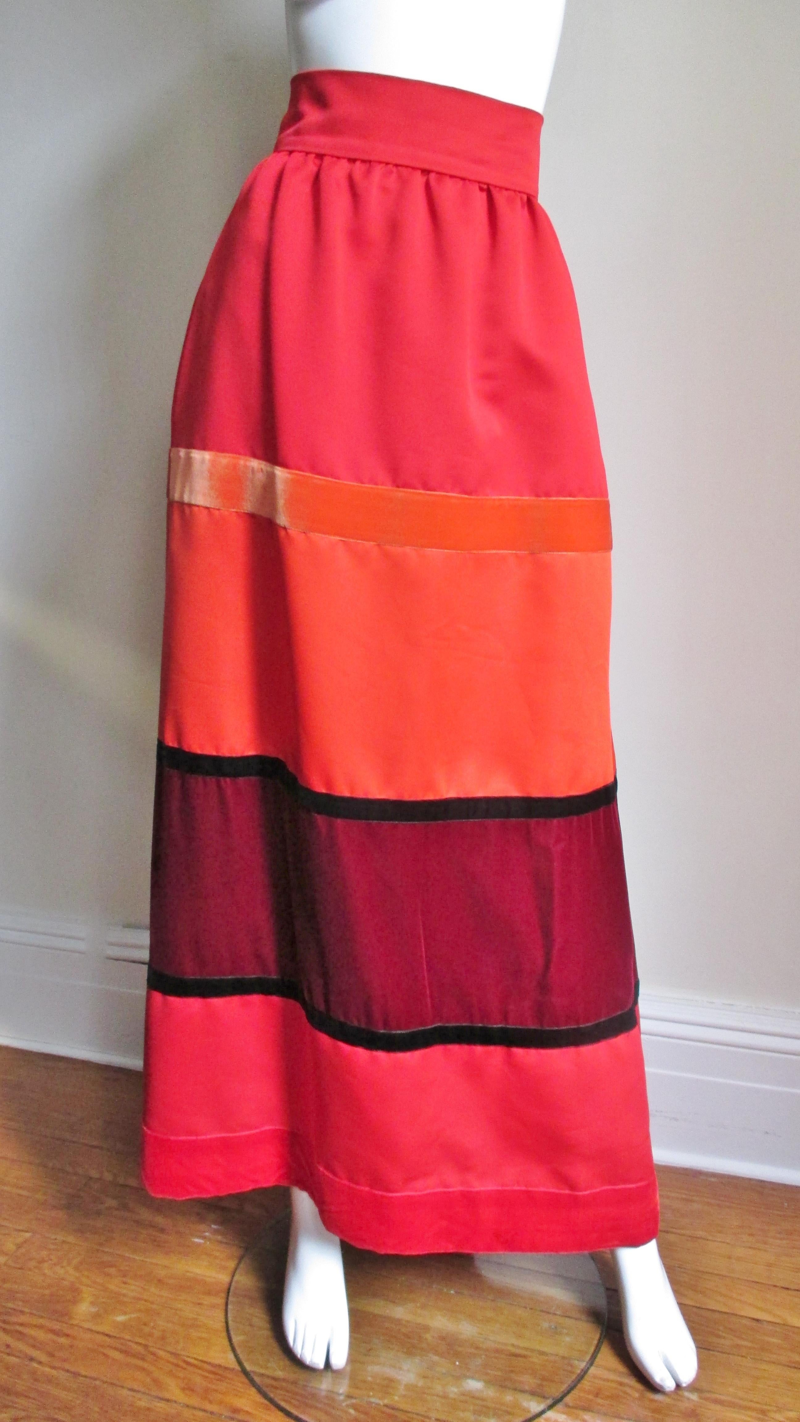 A fabulous maxi skirt in red, orange and burgundy from Malcolm Starr. The skirt gathered onto a waistband has varying widths of horizontal velvet panels in red, orange, burgundy and black.  It has a matching center back zipper, hip side seam pockets
