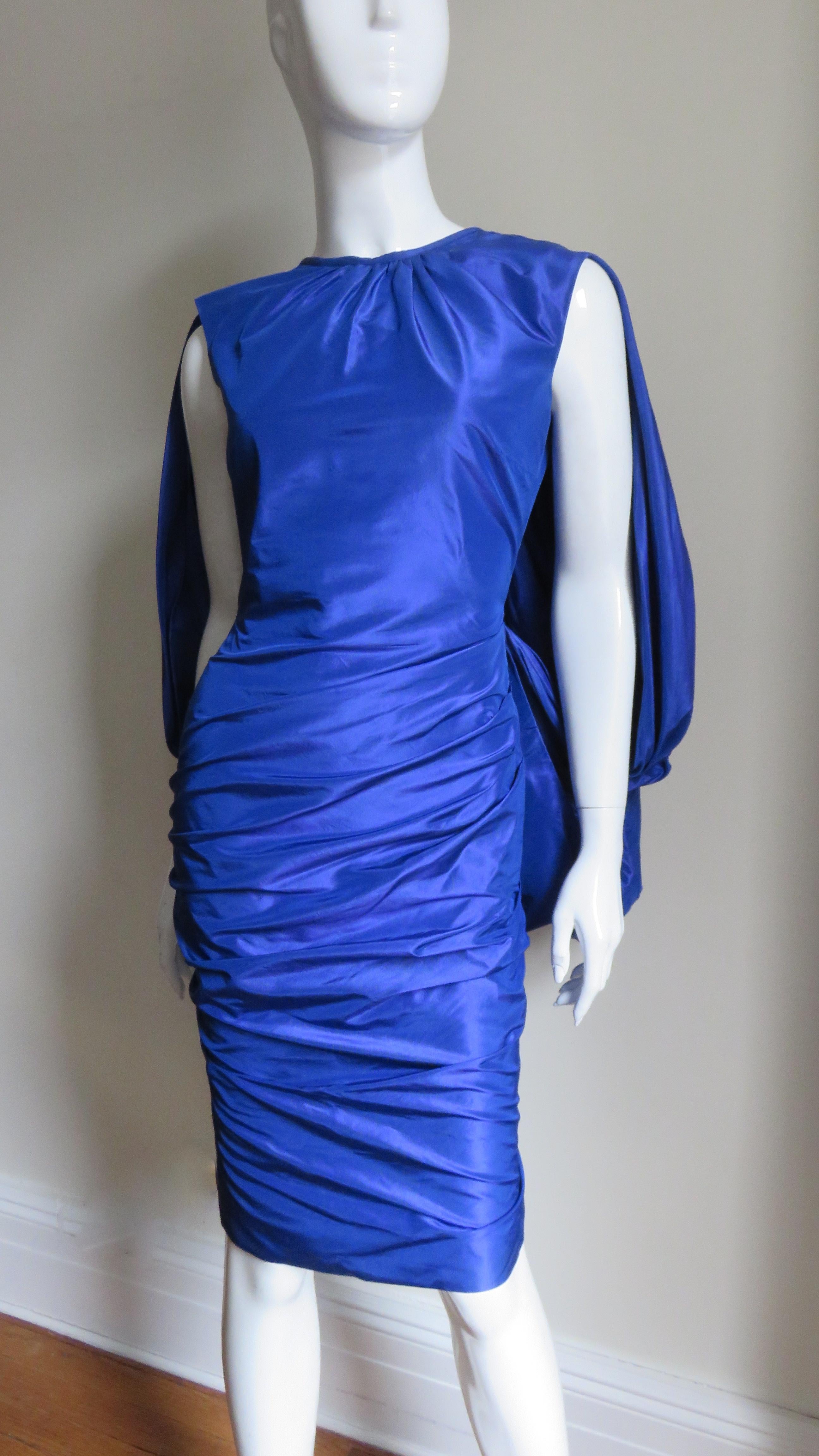 This is a gorgeous cobalt blue silk dress by Tom Ford. It is sleeveless, semi fitted with a horizontally ruched skirt. The back is scooped with a fabulous hip length gathered drape emanating from it creating a cape effect. The dress is fully lined