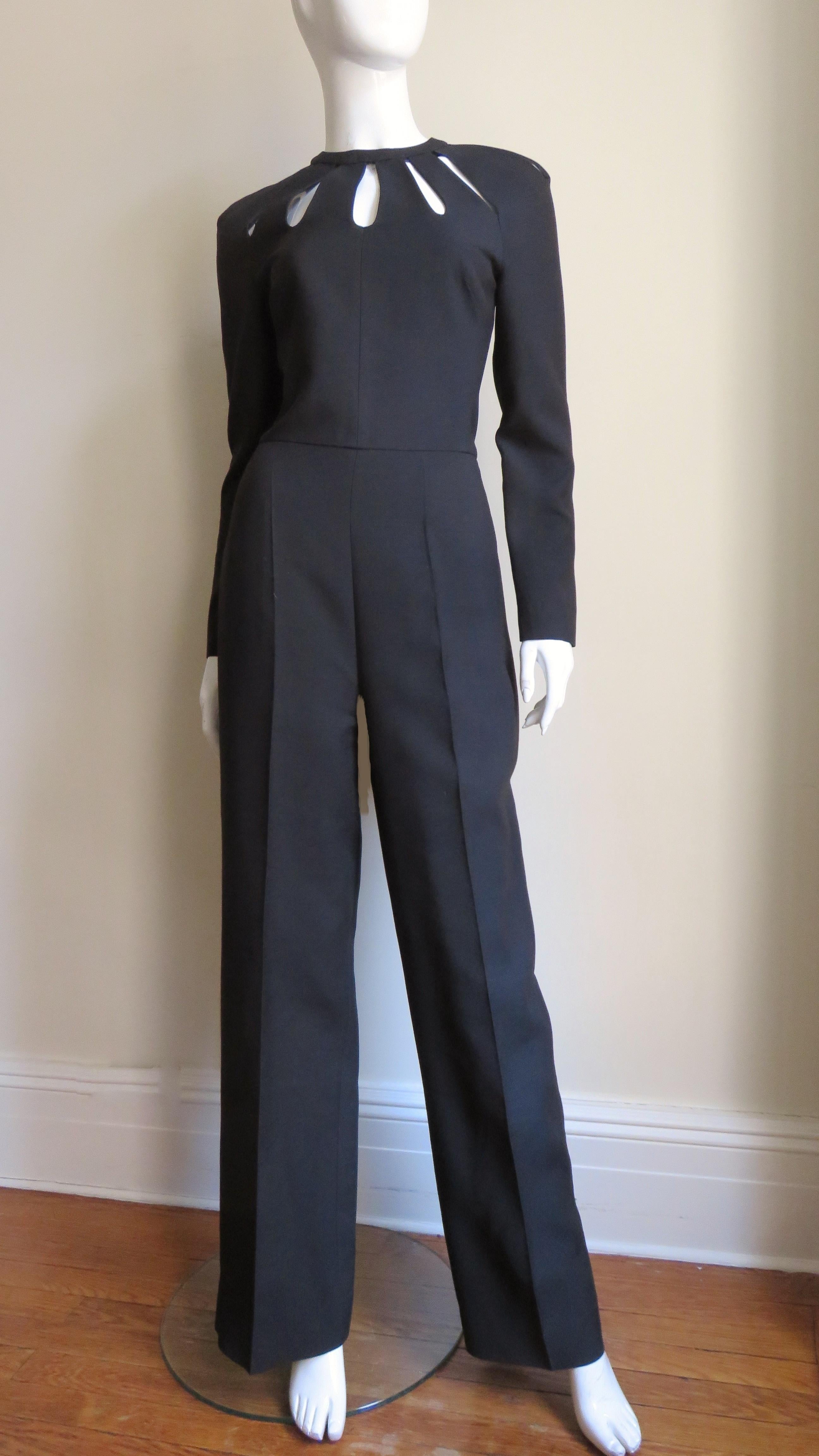 A gorgeous black silk jumpsuit by Valentino.  It is semi fitted with long raglan sleeves, full straight legs and elongated, gradated oval cutouts radiating from the neckline.  It comes with an optional detachable off white leather flower applique