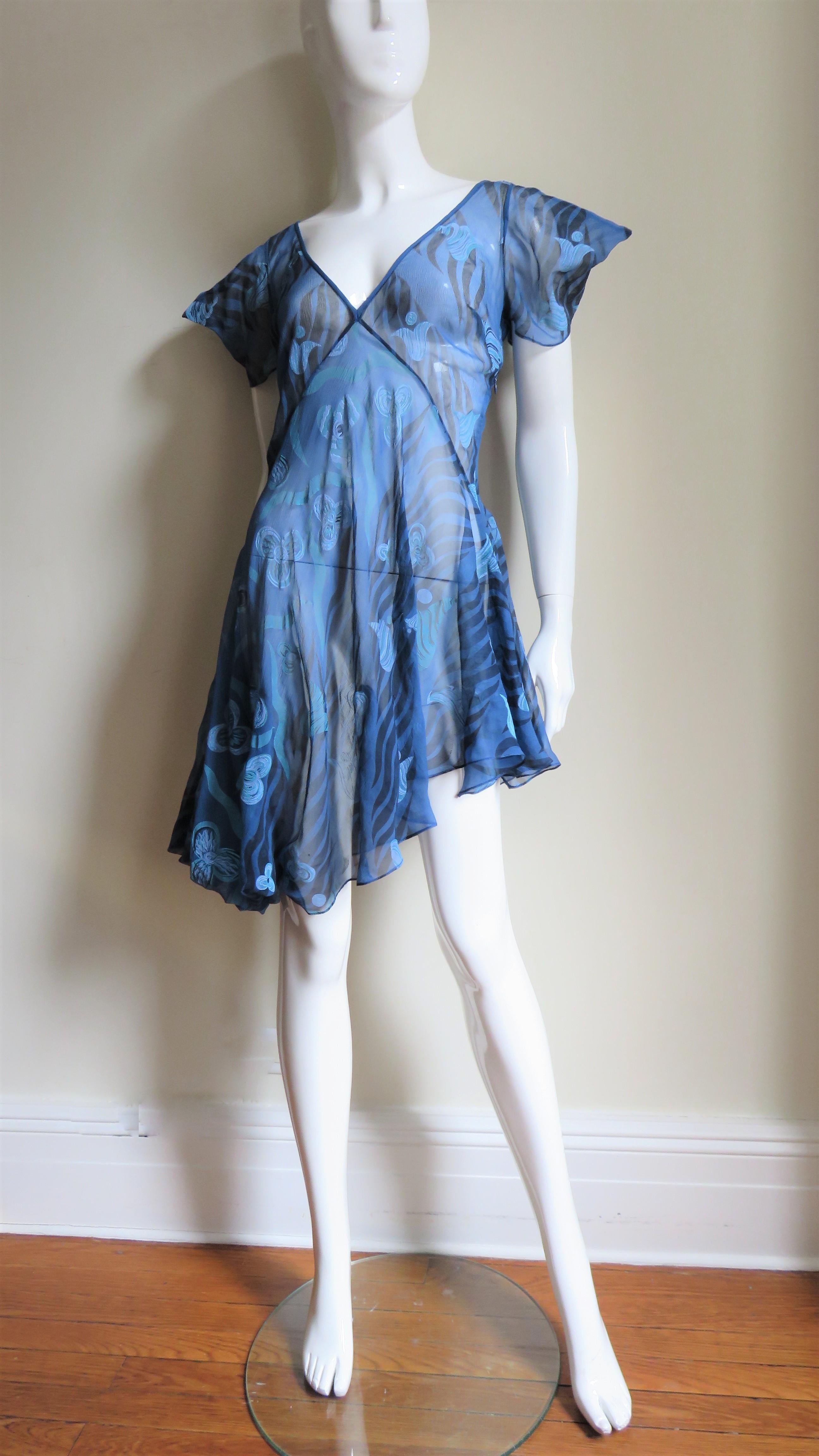 A beautiful blue sheer silk dress in an abstract flower print from Zandra Rhodes. It has a deep V neck and short sleeves accentuated with points.  It is semi fitted through the waist and than flares to the asymmetric hemline.  It is unlined and has
