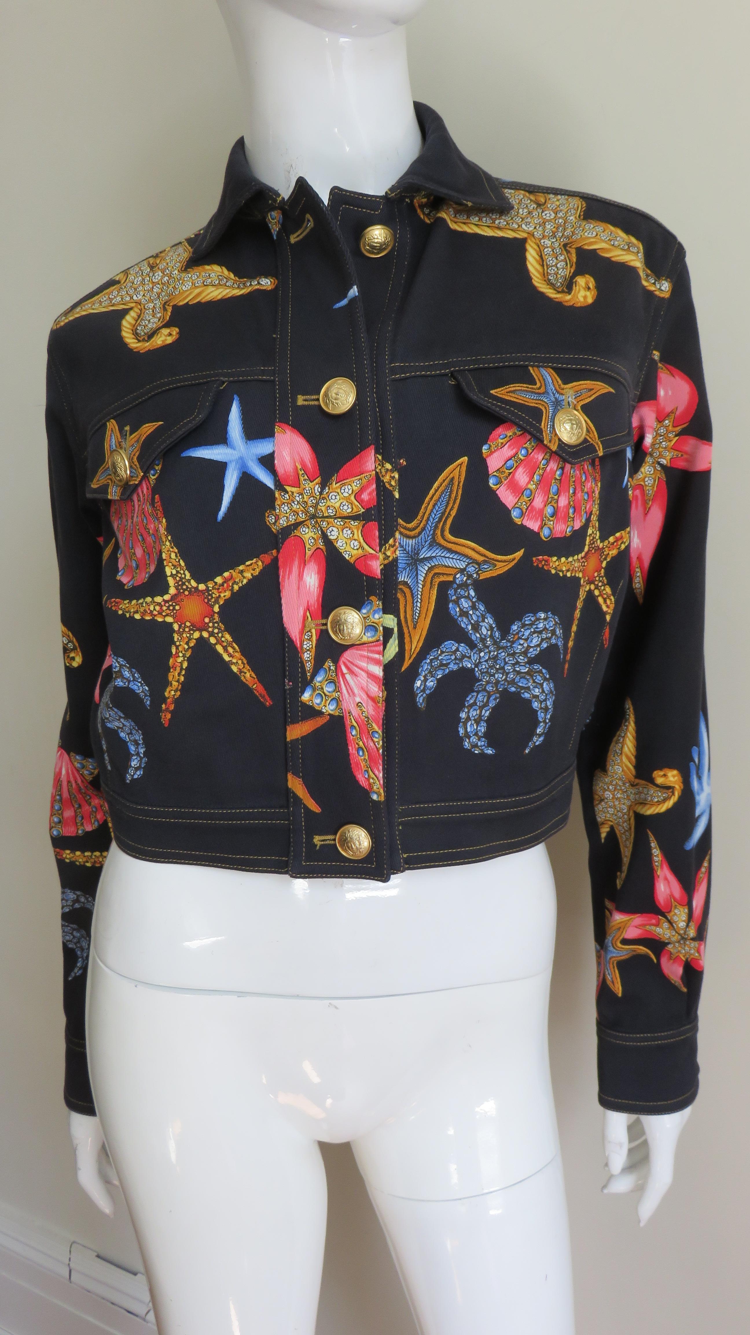 A beautiful black cotton jacket with a colorful starfish and shells pattern from Gianni Versace's much photographed, notable Spring Summer 1992 collection.  It has 2 front flap breast pockets which along with the cuffs and the front of the jacket