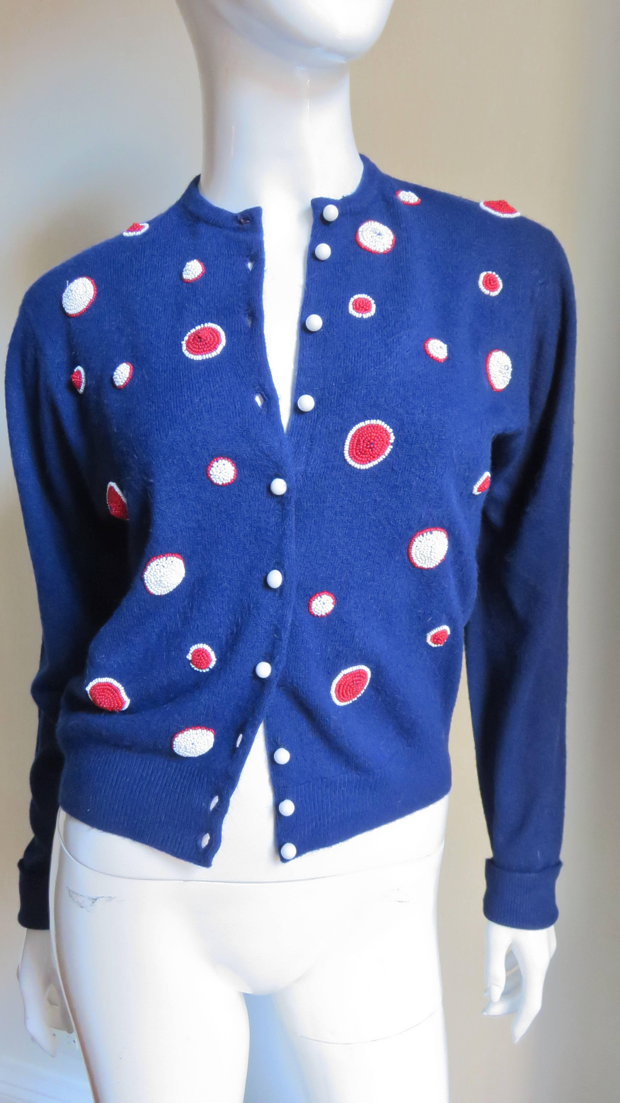 A beautiful beaded blue cashmere cardigan sweater from Elsa Schiaparelli.  The front is decorated with red glass beaded circles of different sizes outlined with white glass beads and the reverse with white beaded circles outlined in red beads all