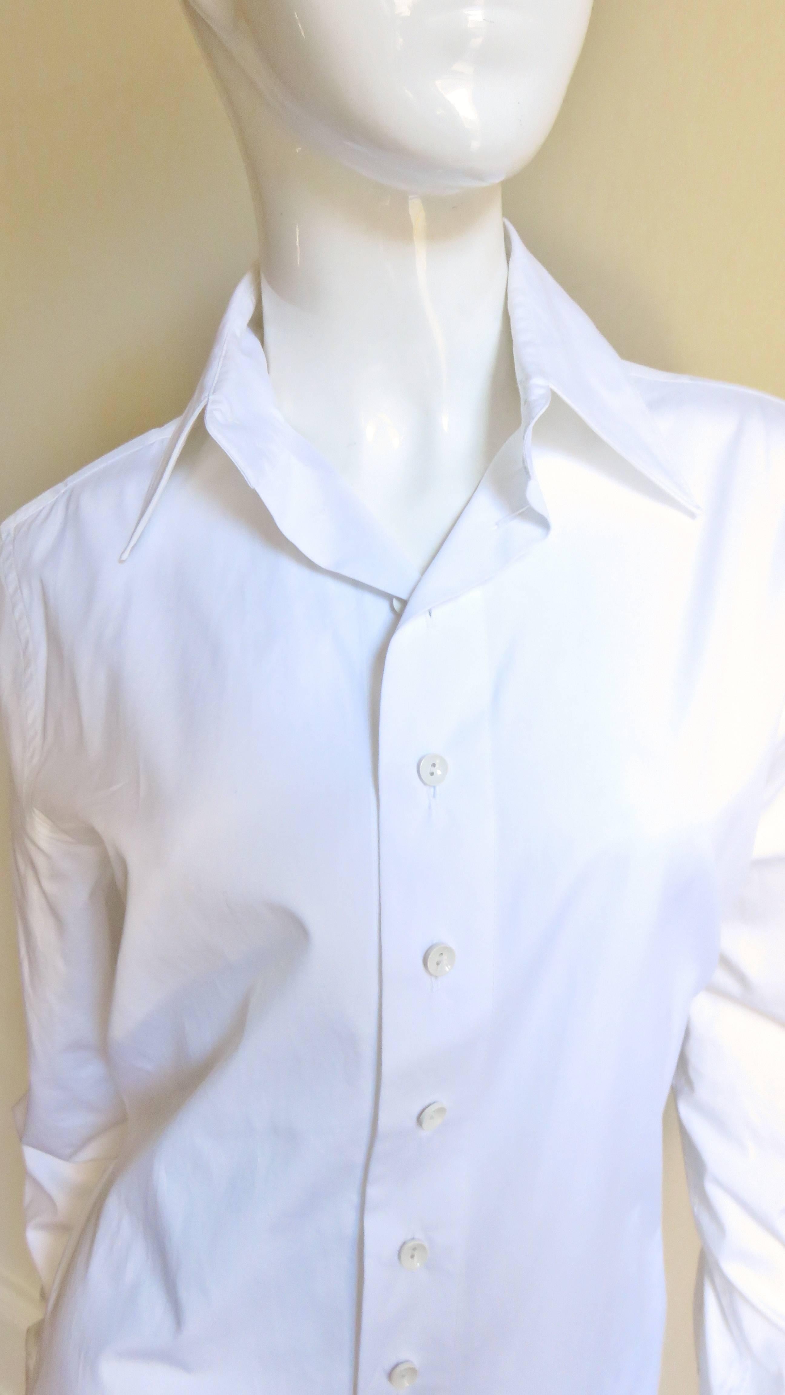 A fabuous white cotton shirt from Jean Paul Gaultier. It is a typical button up front collared long sleeve button cuff shirt with tails but has back drama of an adjustable black stretch band that crosses the waist and back.
Excellent, appears