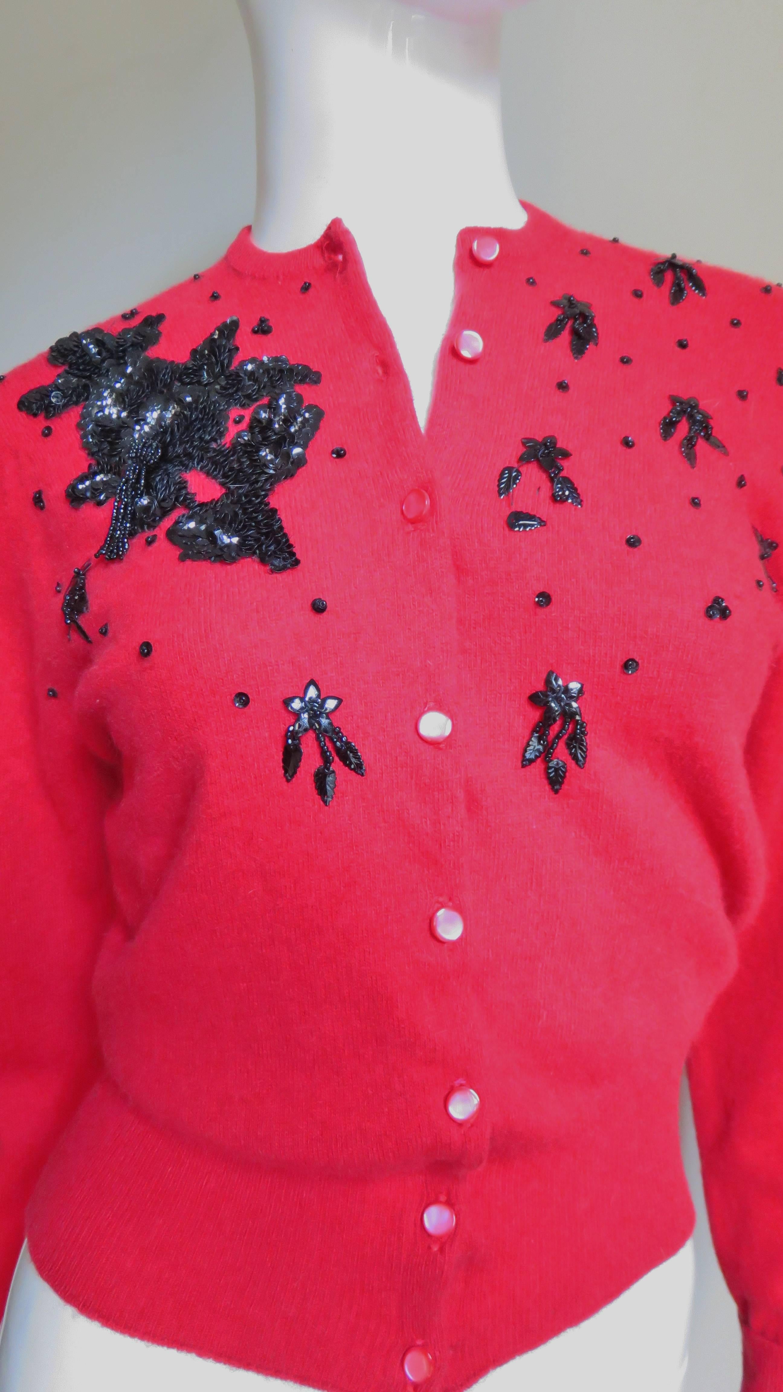 Un magnifique pull cardigan perlé en cachemire rouge riche de Lyle & Scot.  Il a des manches longues avec une encolure, des poignets et un ourlet côtelés.  Il y a des perles de rocaille en verre noir et des paillettes dans un motif abstrait, y