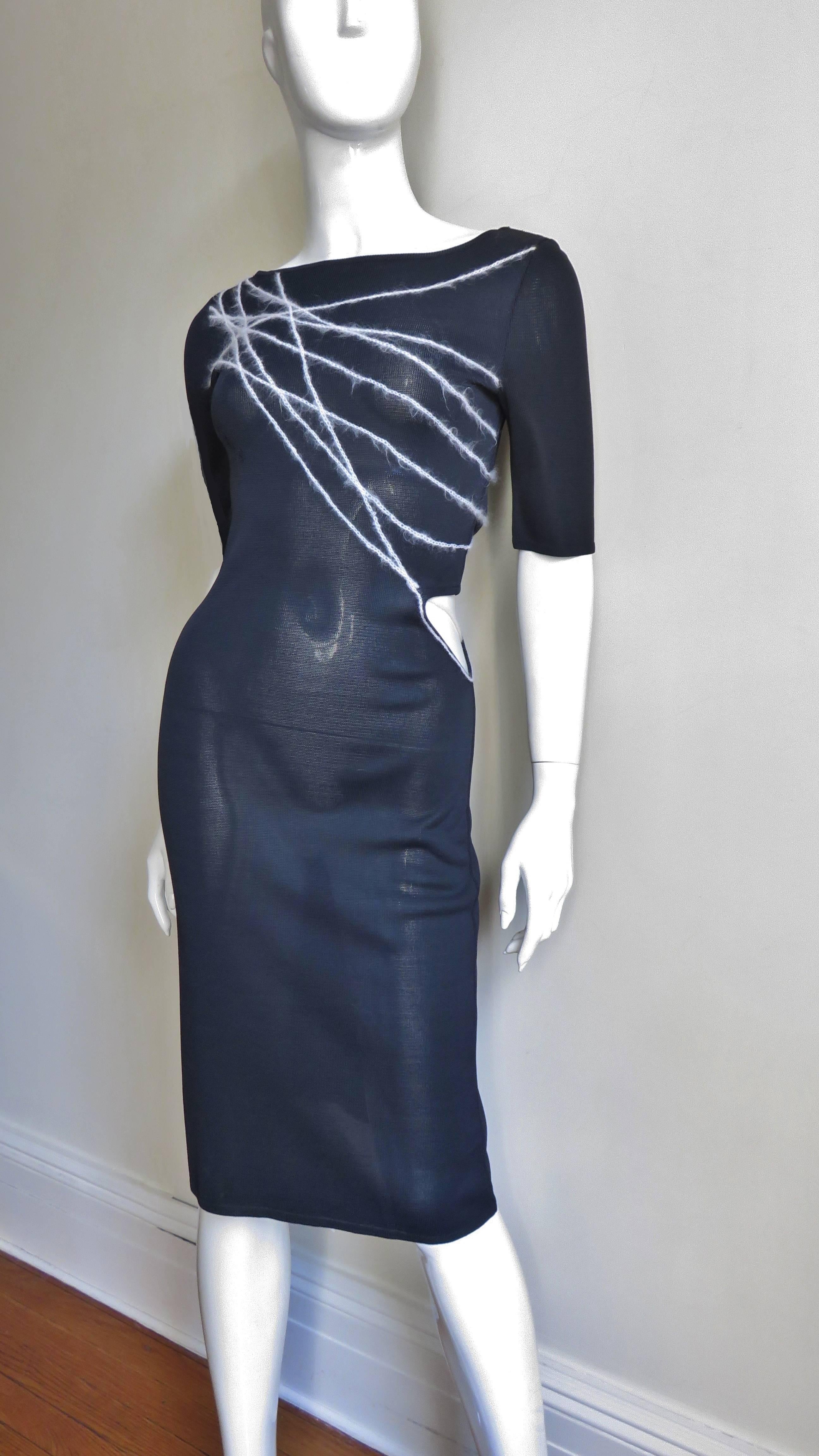 A great black knit dress from Gianni Versace Couture.  It is fitted with a scoop neck, elbow length sleeves and contrasting white lines of yarn abstractly crossing the bodice diagonally front and back.  There is cutout at the waist.  It is unlined