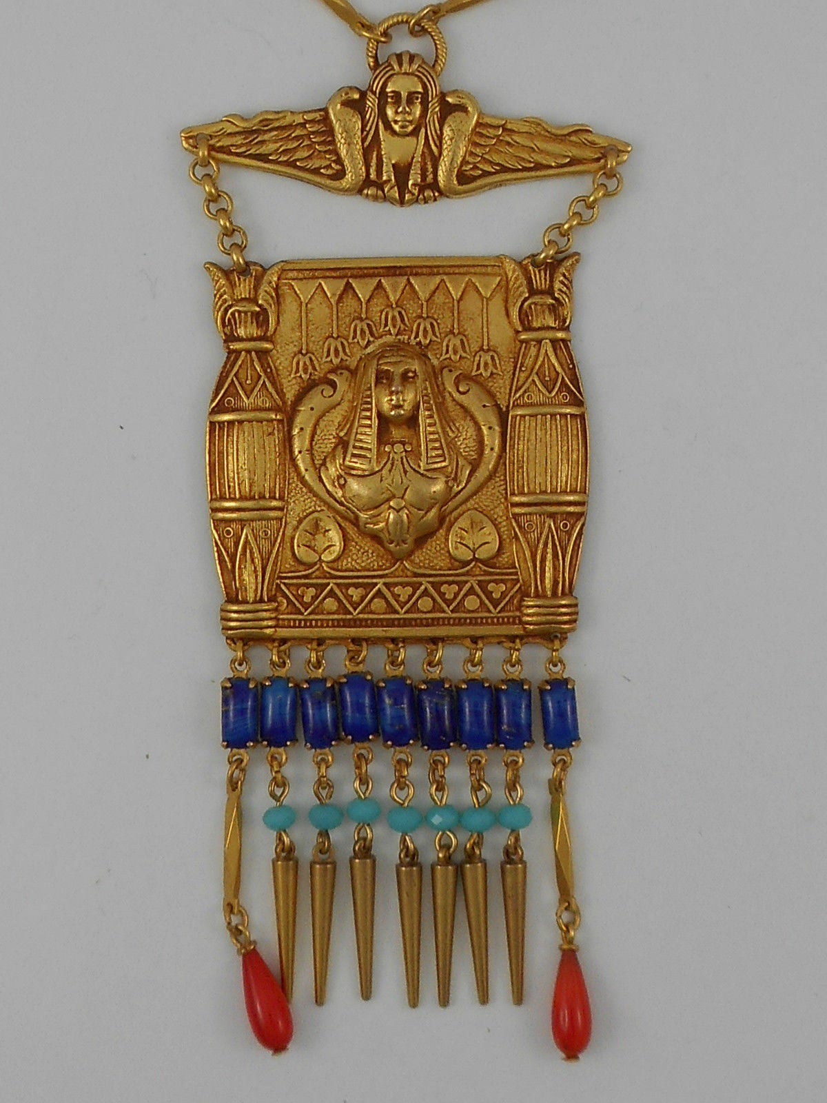 Featuring Askew London Cleopatra and Pillar Designs Rectangular Statement Pendant Necklace; Antiqued Gilt Brass with Fringe Of Blue Glass Baguettes, Faux Turquoise Cushion faceted Beads and Coral Drops. Pendant is suspended from smaller bar and a