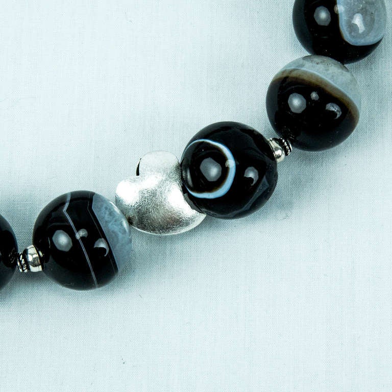Splendida collana di perle di agata nera a bande grandi, composta da 16 perle di agata a bande rotonde di circa 22 mm ciascuna, impreziosite da due cuori e distanziatori in argento sterling. Incordata a mano. La collana misura circa 17 pollici di