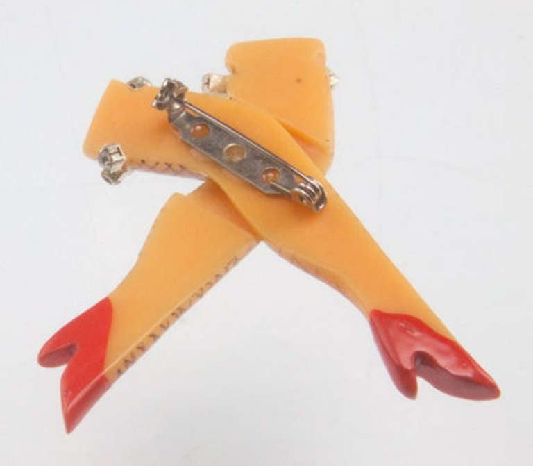 A Wonderful unique pin featuring pair of crossed woman's legs wearing fishnet stockings, rhinestone garters and red high heeled shoes! Inspired by the Art Deco, 1920s-'30s period. Made of Galalith, one of the oldest plastics, a type of Lucite resin.