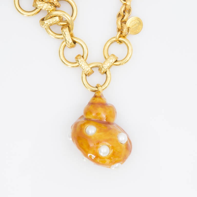Stunning Dominique Aurientis Orange Enamel on Resin Faux Pearl Shell and Gold tone Chain Charm Bracelet with three charms. The gold tone chain is a single strand of round and oval links. The secure closure is a crossbar and loop; the Dominique