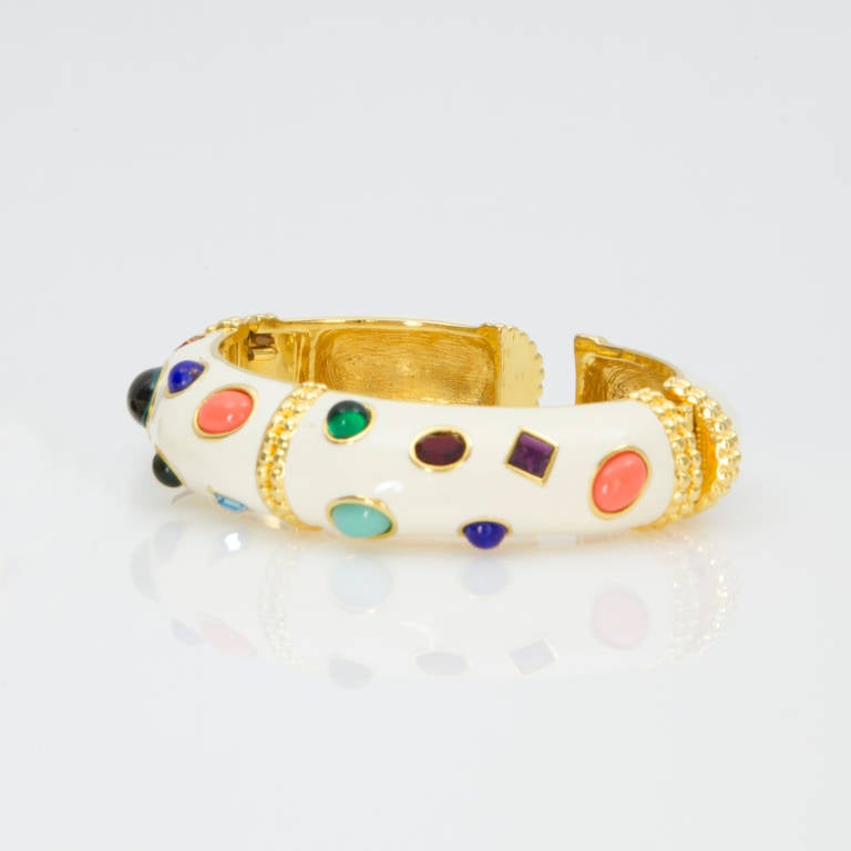 The bracelet and clip on earrings are enamel cream/ivory color on gold tone metal, inlaid with multiple rhinestones and glass domed cabochons, making a striking combination. Each piece is signed KJL on the interior.The bracelet has two hinges, one