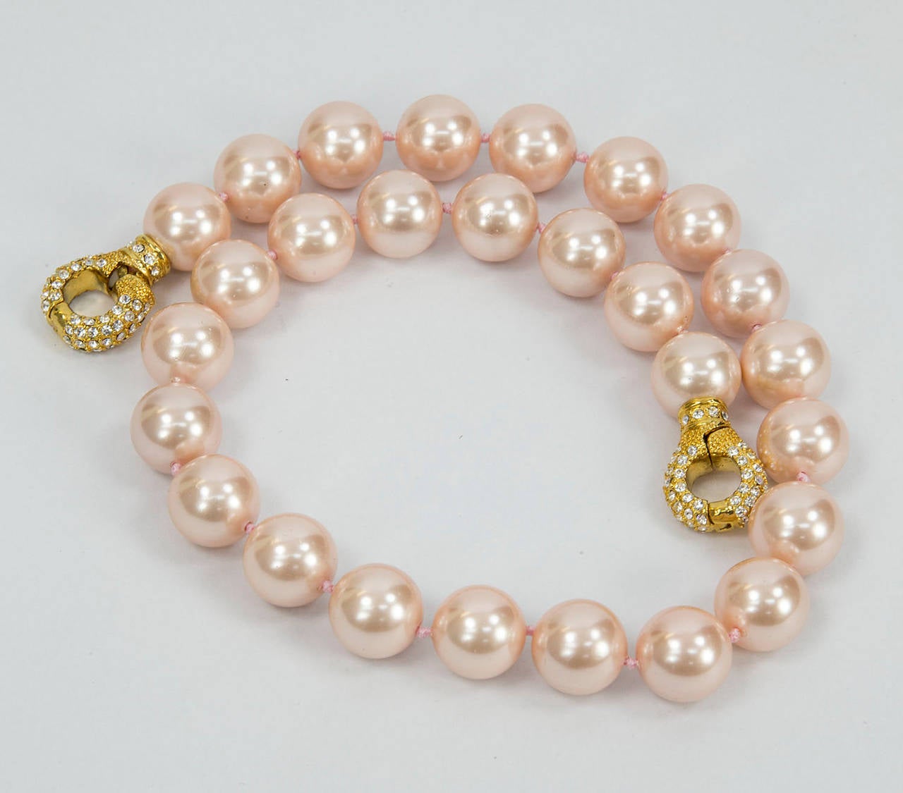 Striking lustrous 14mm Pink Faux Pearl Necklace; hand knotted with matching color silk thread; held by a CZ encrusted interlocking magnetic clasp. Measuring approx .18” long. Go anywhere in style with this Chic and Timeless strand of Pearls! 
