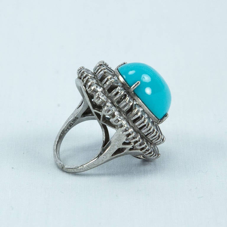 Simply Beautiful! Statement Dujay Cocktail Ring. Centering an oval faux Turquoise, surrounded, on two levels, by baguette and round Sparkling White Zircons on gallery mounting. Marked on shank: STERLING. Ring size 5.75. Approx. size top: 1.25: x 1”.