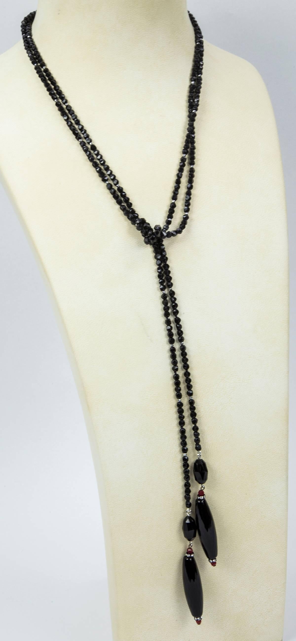 Soft faceted sheen Black Jet Lariat accented by faceted red, silver and Sparkling CZ stones, suspending two large faceted elongated teardrop shaped Jet glass beads, each measuring approx. 2” in length; approx. length of necklace: 65”. So