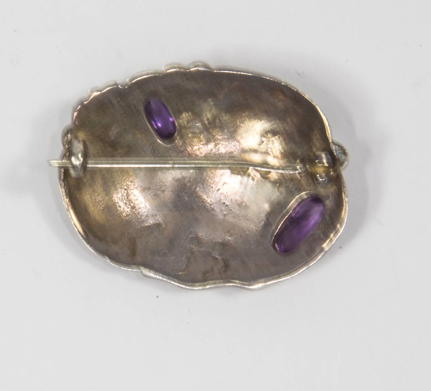 Seltene ovale Jugendstil-Brosche aus Sterlingsilber von Fahrner, in der Mitte mit zwei Amethysten besetzt, umgeben von geprägten Lilienblättern. Unterzeichnet: TF im Kreis für: Theodor Fahrner und 935; ca. Anfang 1900 Pforzheim, Deutschland. Schick