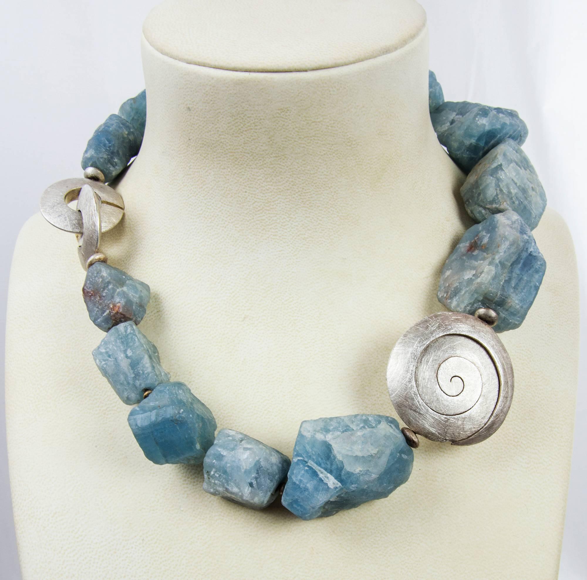 Large graduated Natural organic Aquamarine nuggets, accented with a large textured Sterling Silver swirl rondelle, inter-spaced with S/S spacers and held by a round S/S textured clasp comprising this mesmerizing necklace. Approx. necklace length