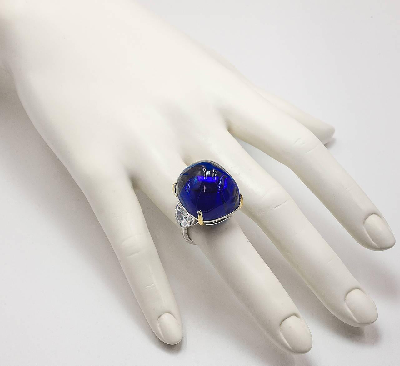 Superb faux French pyramid-cut cabochon Royal Kashmir Blue sapphire half-moon cubic zircon set white gold ring. The faux  man made sapphire has the look of about 40 carats and the side stones about two carat diamond weight each. Faux sapphire 