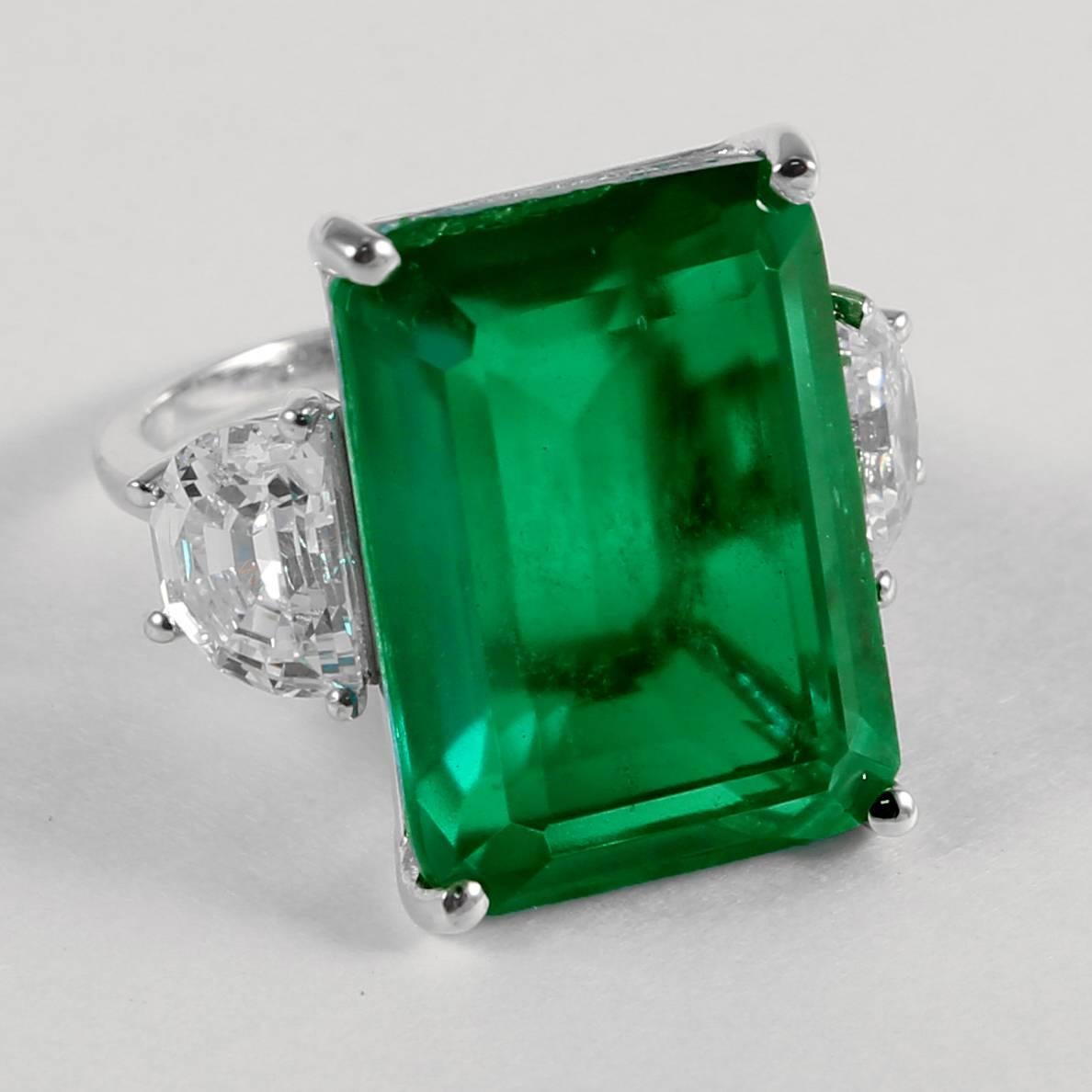 Magnificent faux 25 carat rectangular step cut emerald made of the finest green 
natural material faux emerald set with half moons either side in white gold. This ring has an amazing warm glow. Measures 1inch long and 3/4inch wide.
Free sizing.
