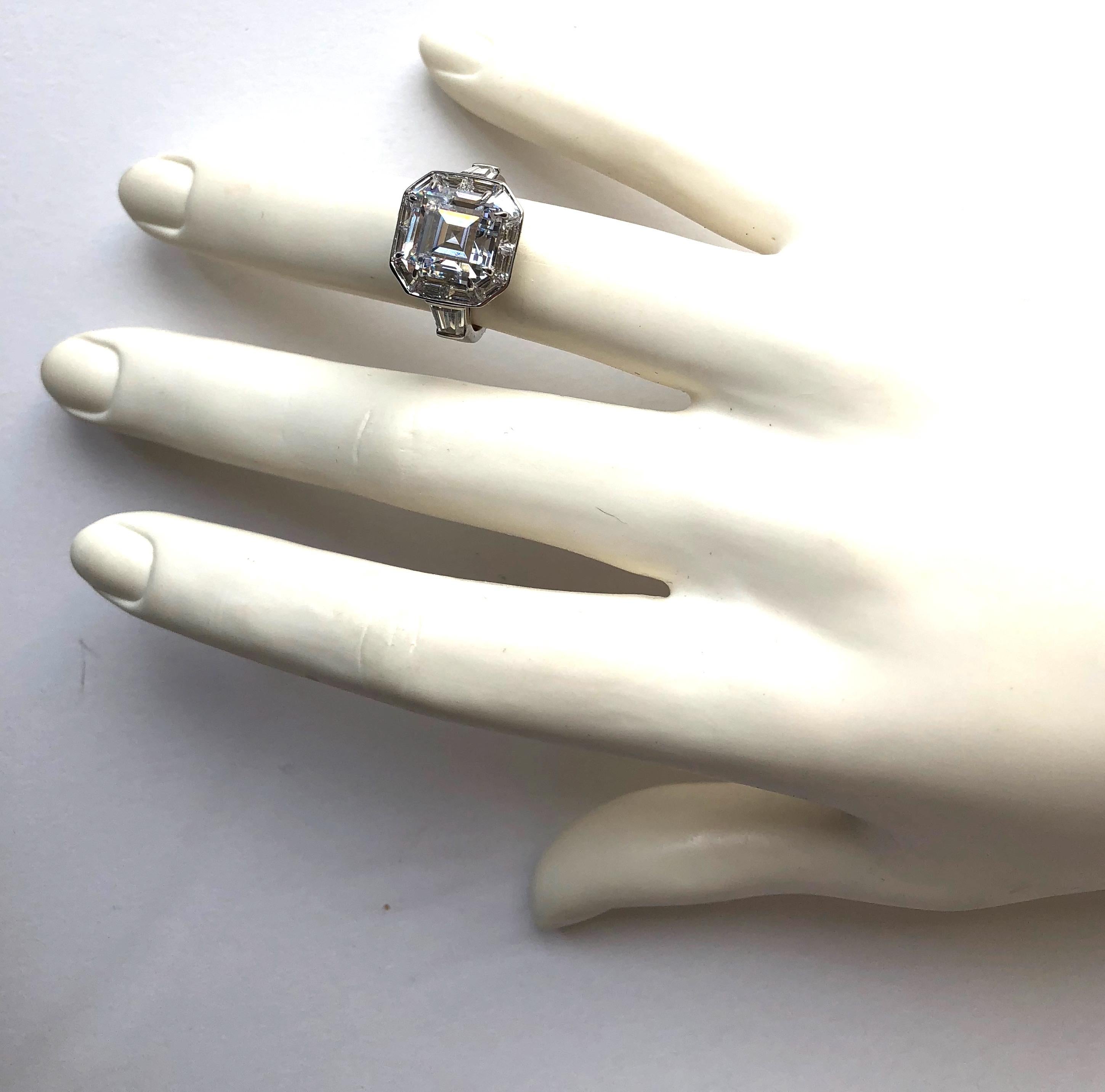 Magnificent Costume Jewelry Art Deco Style Square Cubic Zirconia Diamond Halo Style Silver Ring Bordered with Cubic Zirconia Fancy-Cut Baguettes and Tapers on the Shank. 
Center 'diamond' looks a like a 5 carat, bright and sparkly. The ring measures