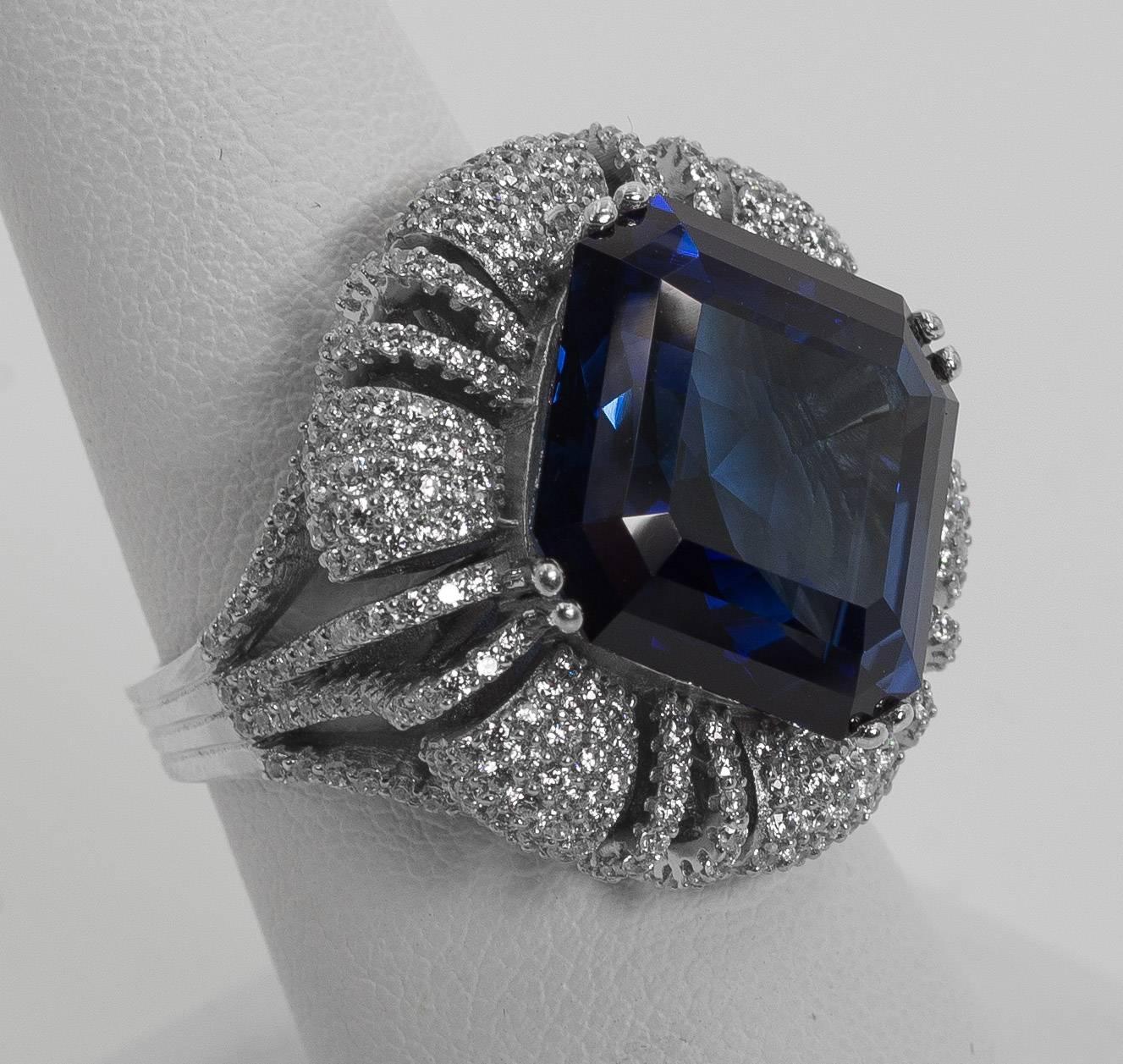 A 10 carat hand cut special emerald cut faux Kashmir color sapphire  nestled on a cushion of pave white cubic zirconia diamonds set in sterling designed to the highest fine standards possible. A classic amazing sparkly and brilliant look that will